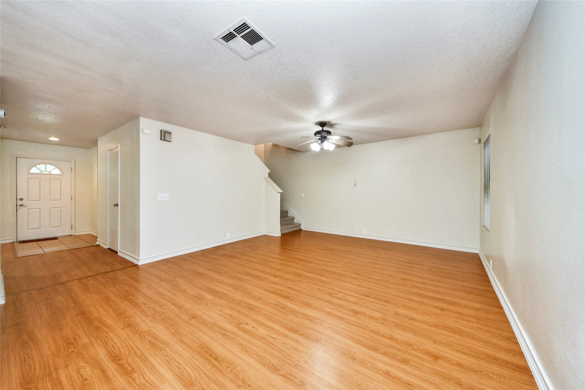 Spacious family room with warm wood flooring, accented by a ceiling fan, offers a welcoming space for relaxation and gatherings.