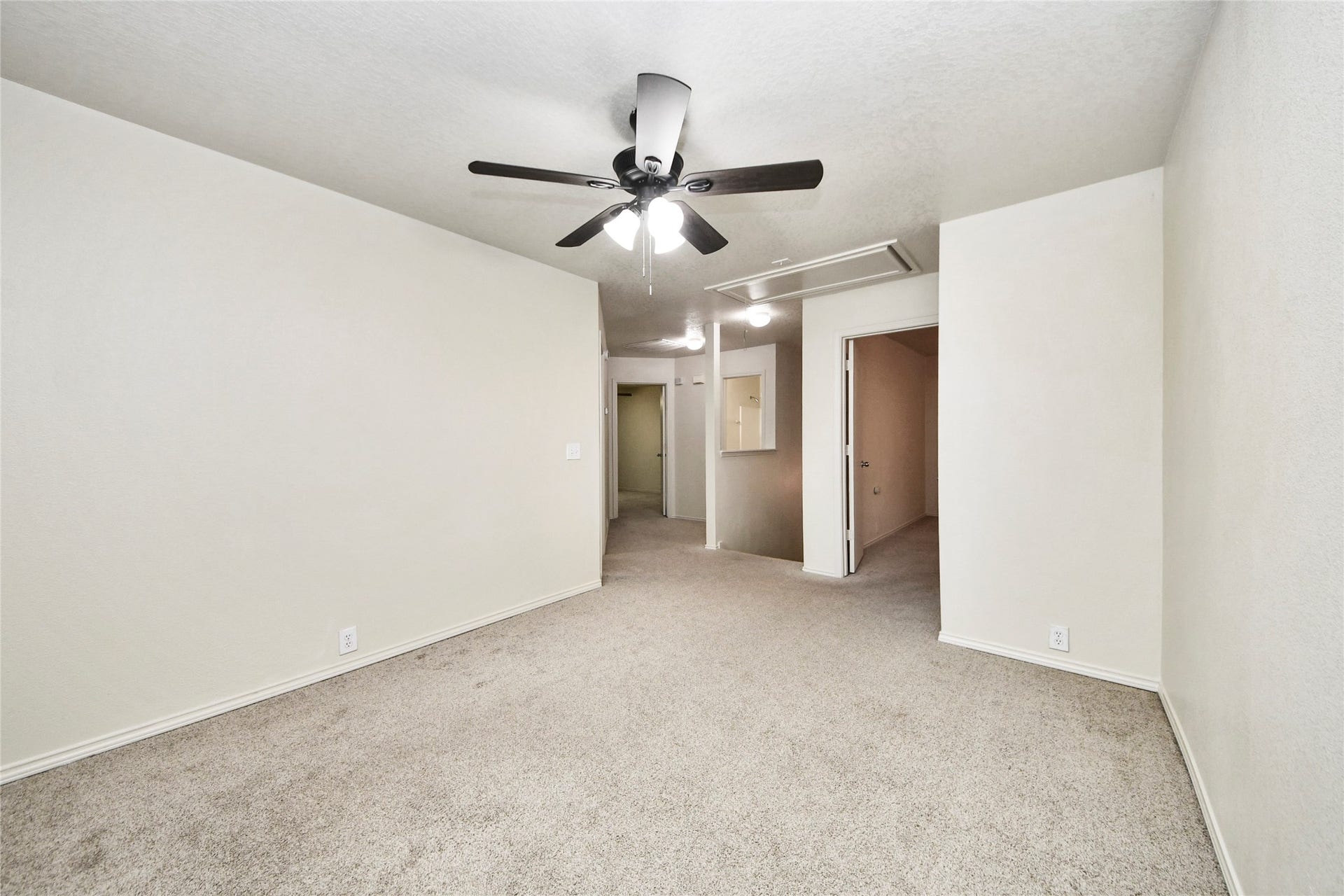 Spacious game room with neutral tones, plush carpeting, and a ceiling fan, perfect for entertainment and relaxation.