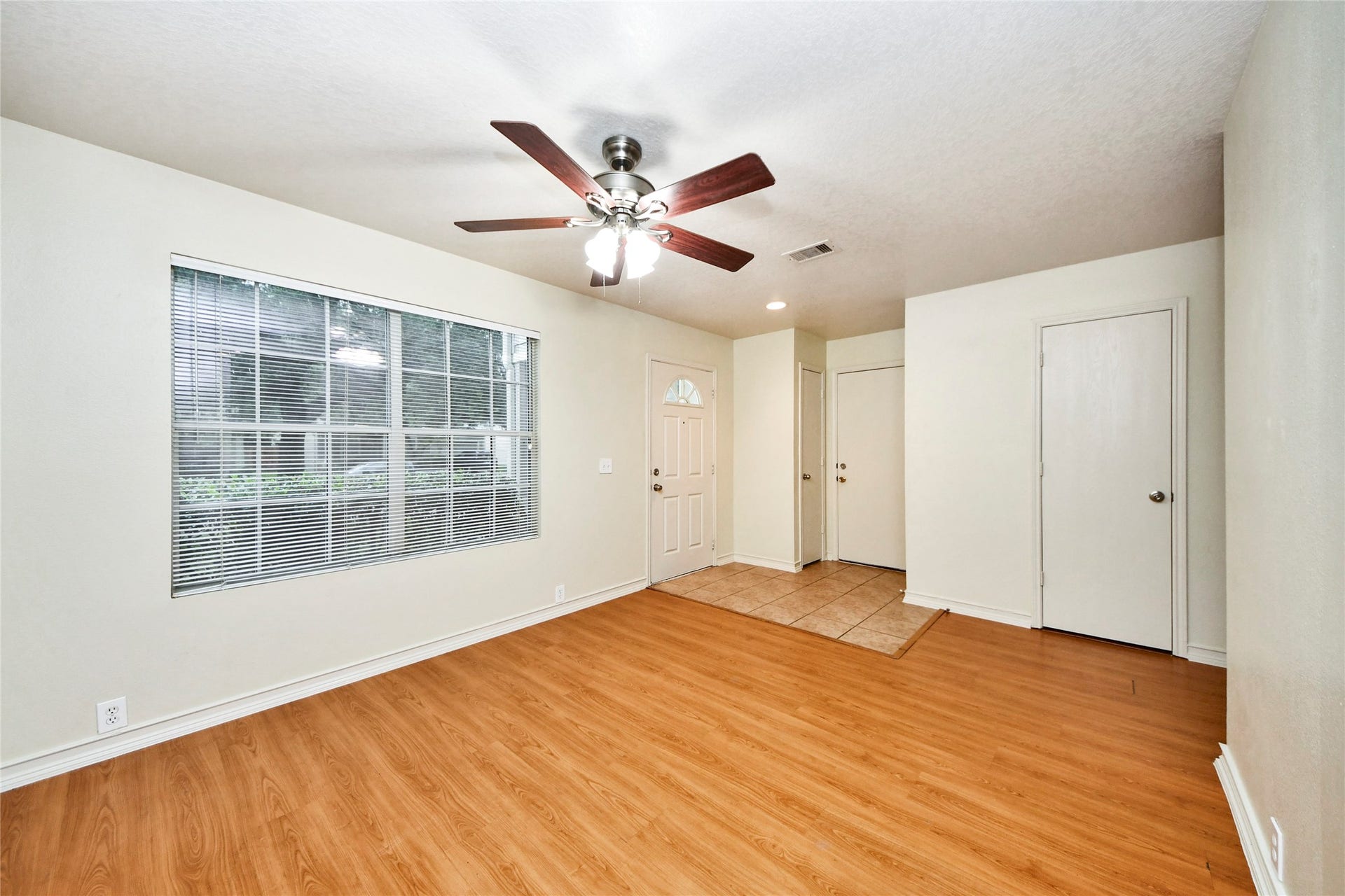Experience cozy living in this inviting den, featuring warm wood flooring, abundant natural light from a large window, and a stylish ceiling fan for ultimate comfort.