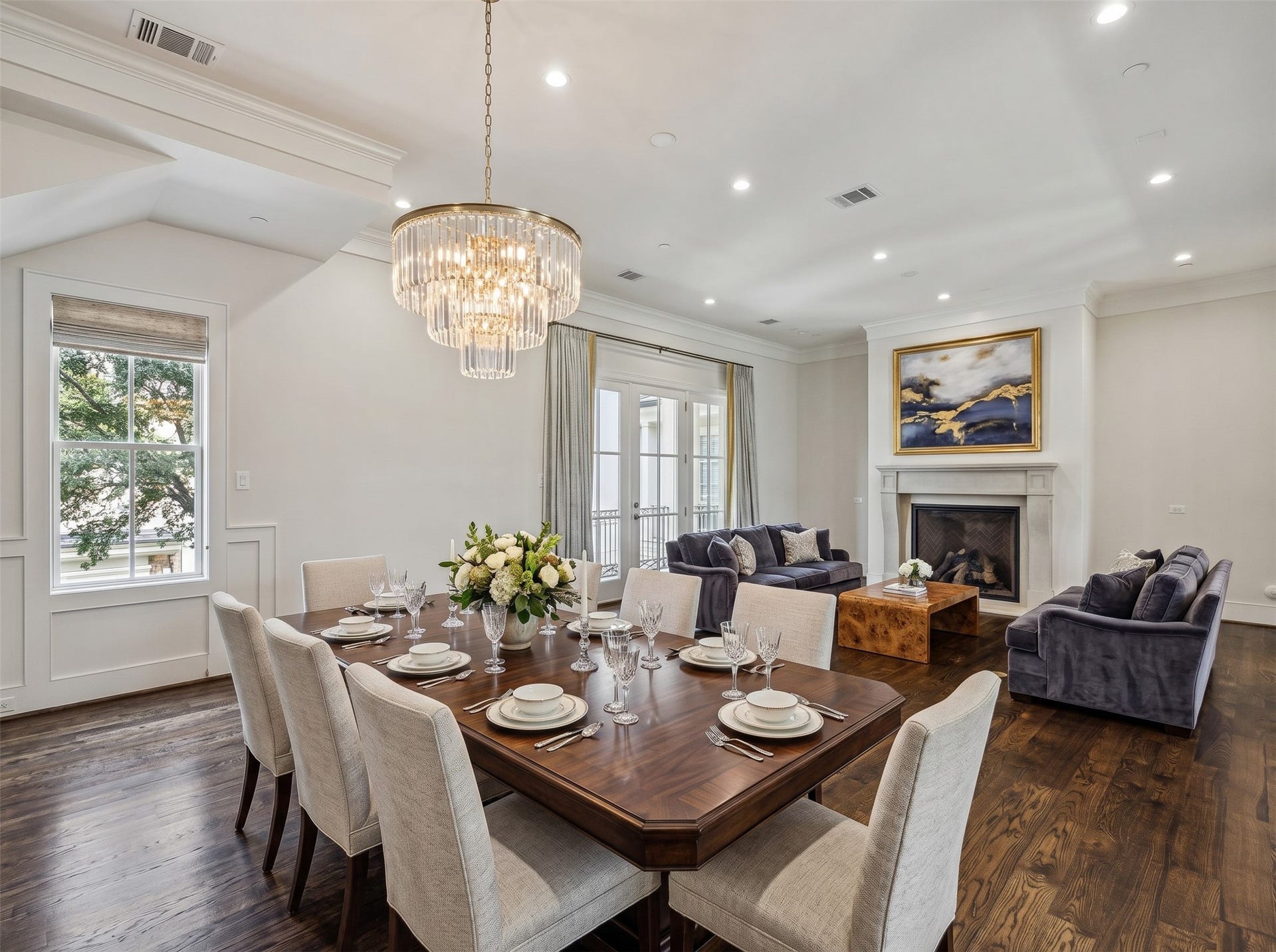 2413 Mimosa Drive, Houston, TX 77019 A second virtually staged view shows just how naturally the living and dining areas can coexist. The fireplace anchors one end while the dining area sits beneath a statement chandelier, with French doors opening directly to the balcony beyon