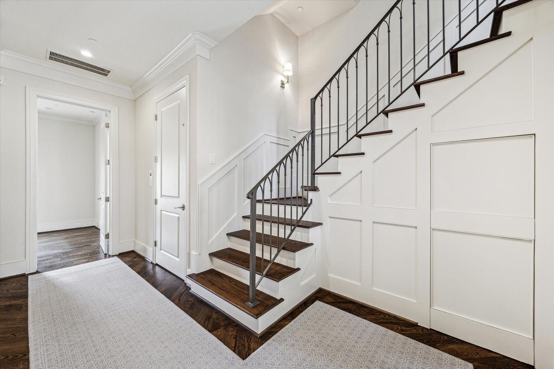 2413 Mimosa Drive, Houston, TX 77019 Just inside, dark hardwood floors and crisp millwork frame the entry, while the staircase introduces one of the homes recurring architectural details: slender ironwork set against warm wood treads and bright white paneling.