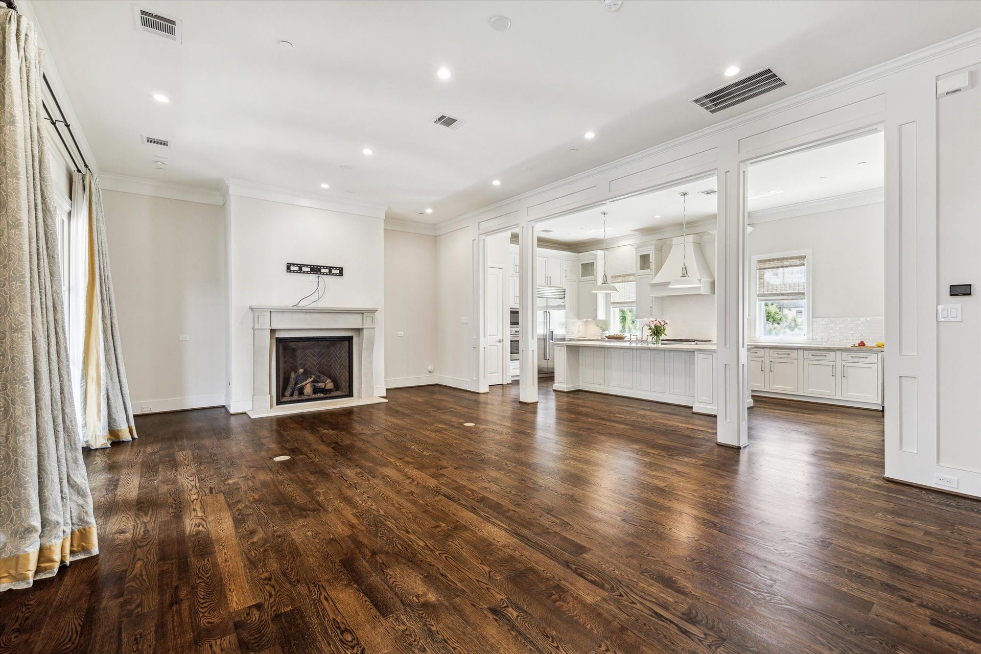 2413 Mimosa Drive, Houston, TX 77019 The main living level is expansive without losing its sense of definition. Rich walnut floors run beneath soaring ceilings, while a fireplace anchors the room and wide architectural openings create an easy transition into the kitchen.