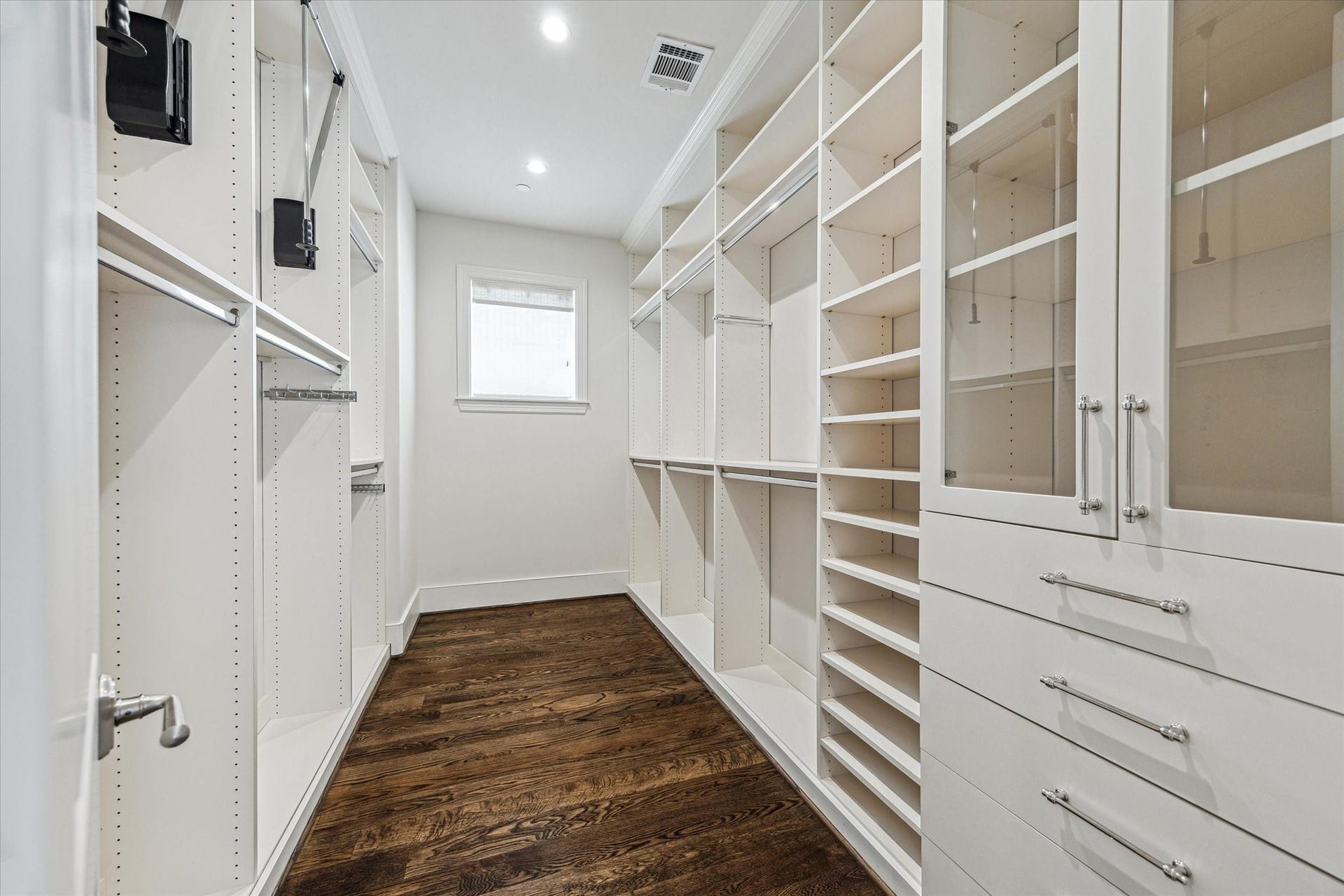 2413 Mimosa Drive, Houston, TX 77019 One of two custom walk-in closets serving the primary suite, this space is fitted from floor to ceiling with hanging storage, open shelving, shoe storage, drawers, and glass-front cabinetryall while leaving a generous center aisle.