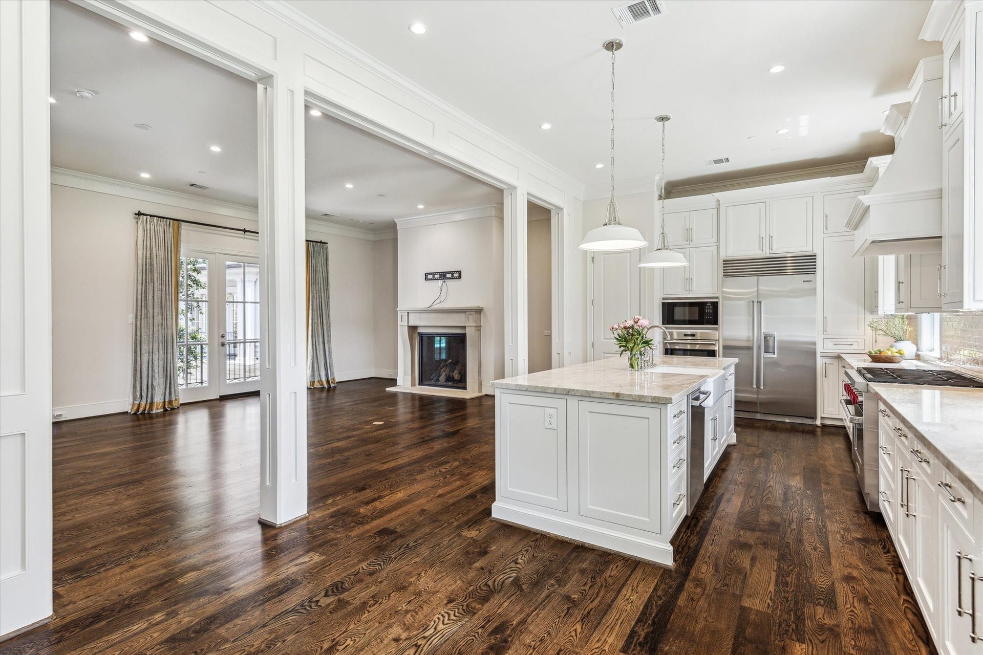 2413 Mimosa Drive, Houston, TX 77019 This view captures the rhythm of the entire main floor. The kitchen stretches from a generous island to extensive perimeter cabinetry and stainless appliances, while broad openings lead directly into the fireplace living area beyondan arrangement designed for the way people actually gather.