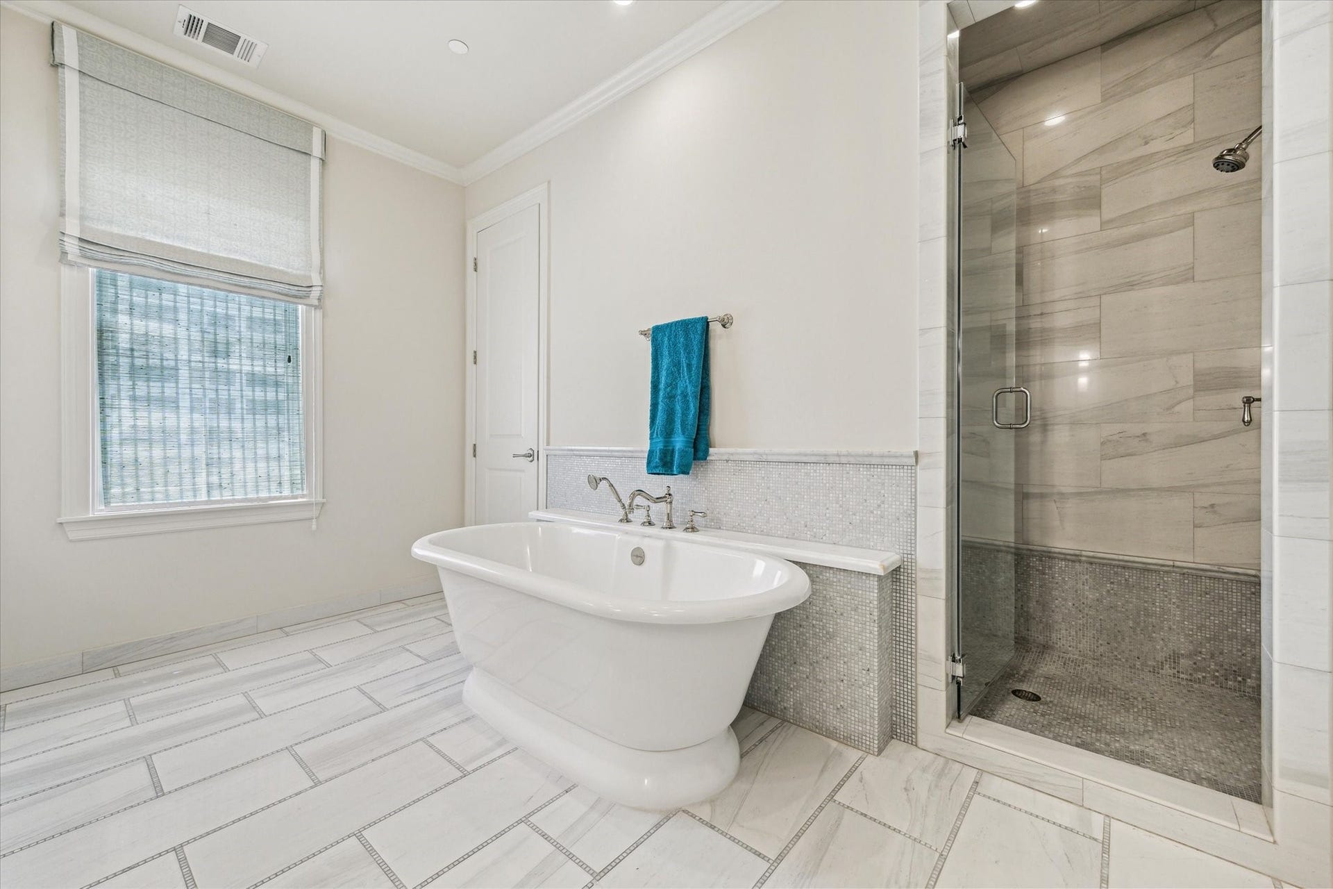 2413 Mimosa Drive, Houston, TX 77019 Opposite the vanity, the bath transitions into a more spa-like setting with a freestanding soaking tub and oversized glass-enclosed shower. Marble-look tile, mosaic detailing, and a built-in shower bench give the space a polished, cohesive finish.