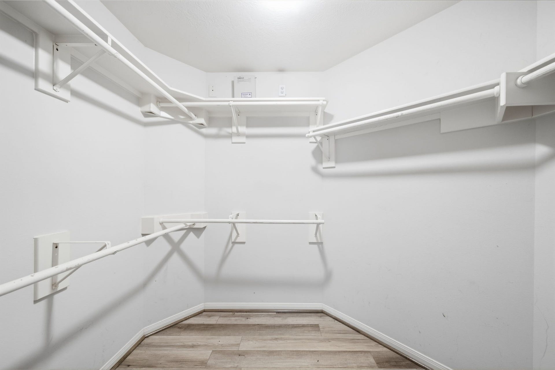 Ample built-in shelving and multi-level hanging rods maximize storage potential in this expansive primary walk-in closet, complete with durable wood-look flooring.