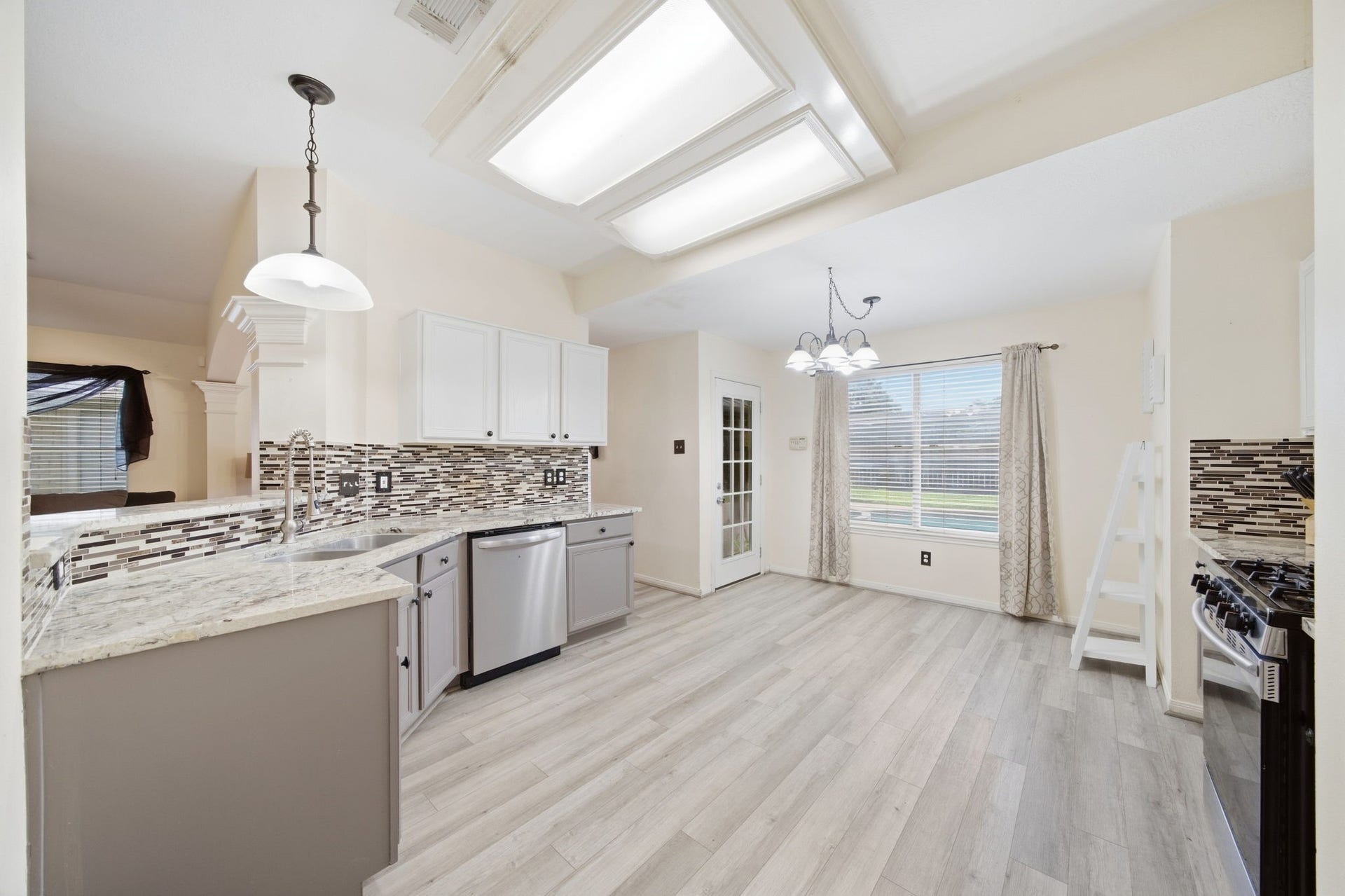 Sunlight fills the casual breakfast area, where durable wood-look flooring extends toward a French door granting direct backyard access. Seamless proximity to the granite kitchen counters and stainless dishwasher ensures effortless meal service and everyday functionality.