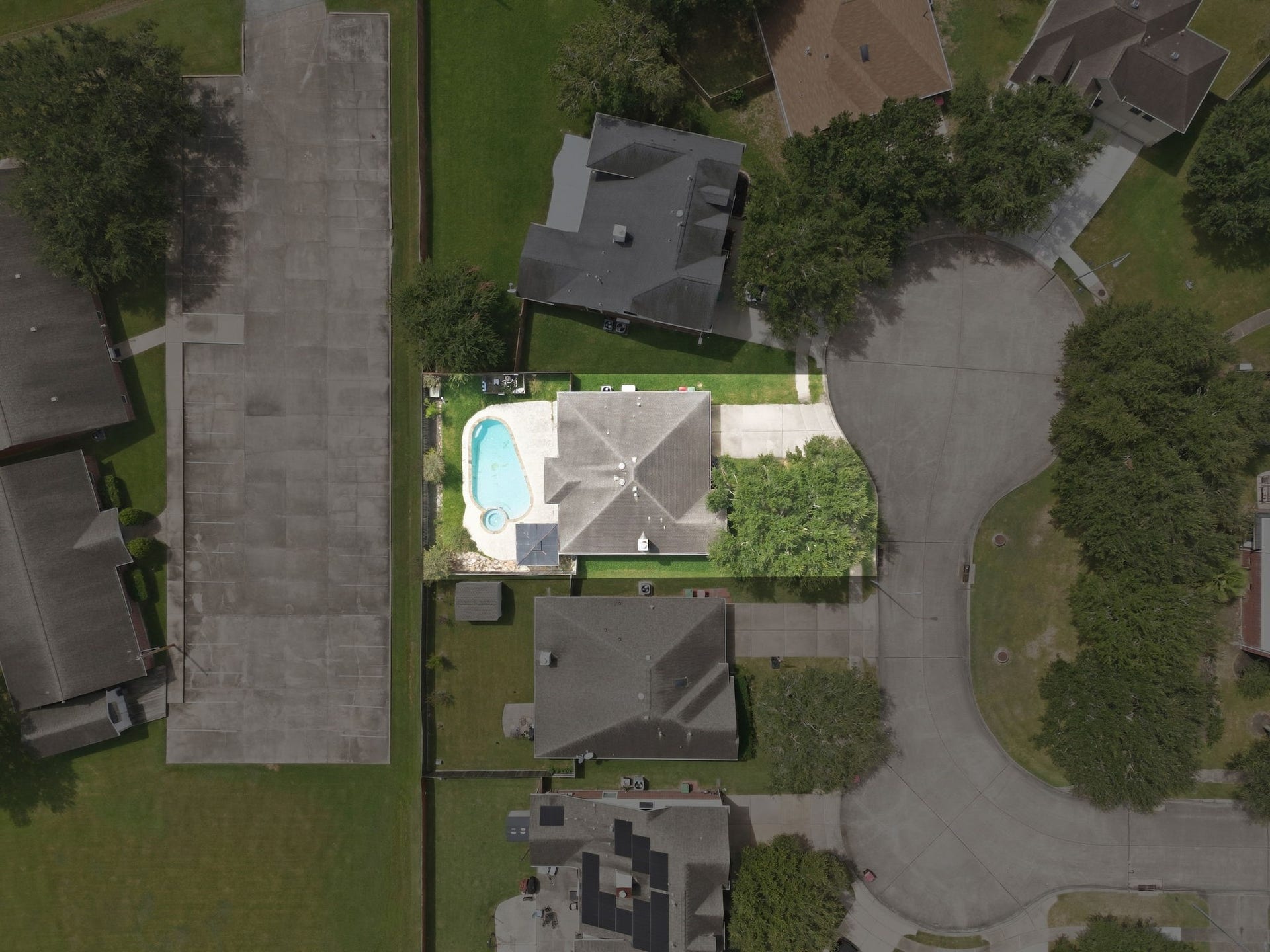 Perched at the head of a cul-de-sac, an overhead view captures the complete footprint of the single-story home, private driveway, and enclosed backyard retreat. The fenced grounds showcase a private in-ground pool, spa, shaded pergola, and storage shed, bordering an open green expanse that eliminates rear neighbors.