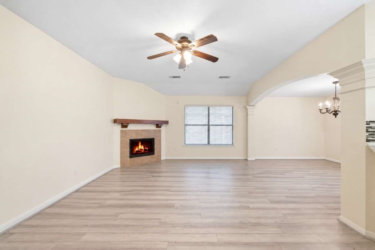 Generous square footage and low-maintenance wood-look flooring define this open living space, centered around a cozy corner fireplace with a rustic wood mantle. Wide arched openings lead into the formal dining room, enhancing the flowing first-floor layout for relaxed everyday entertaining.