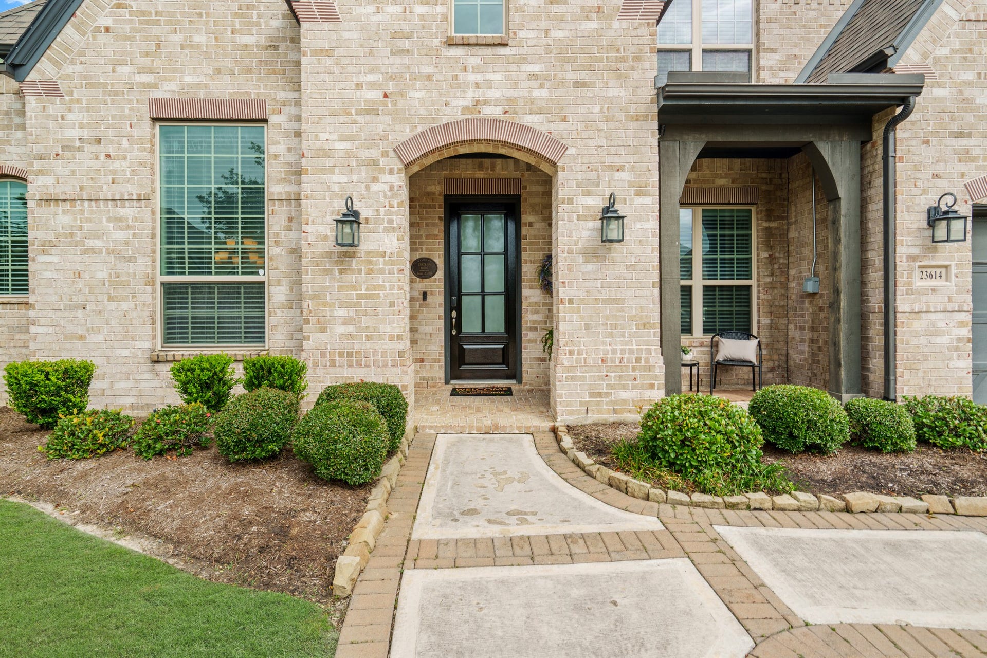 Up-close look at the elegant covered front entryway, highlighting the stately arched brickwork, premium wood pillars, and a modern custom front door with privacy glass.