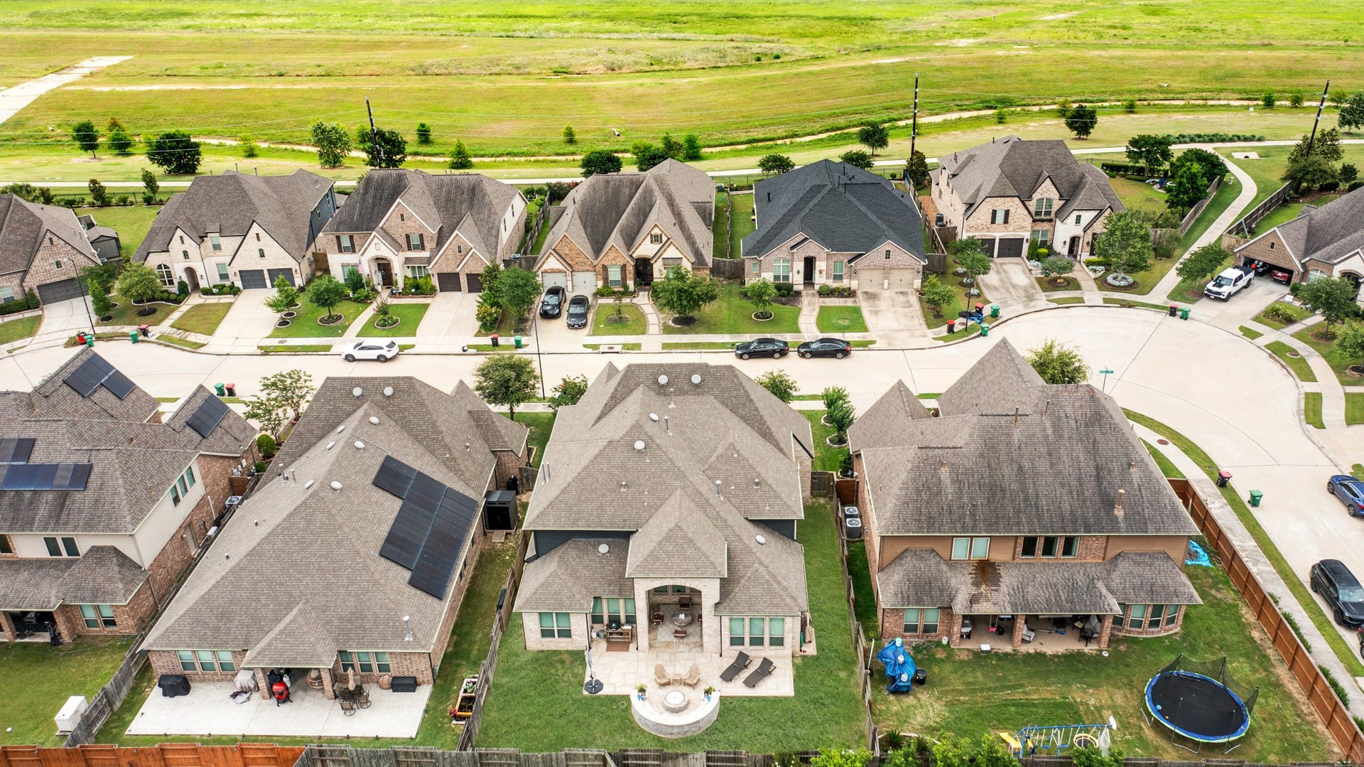A bird's-eye aerial view shows the complete backyard layout, detailing the spacious green lawn, the custom stone firepit, and the home's proximity to Elyson's open green spaces and walking trails.