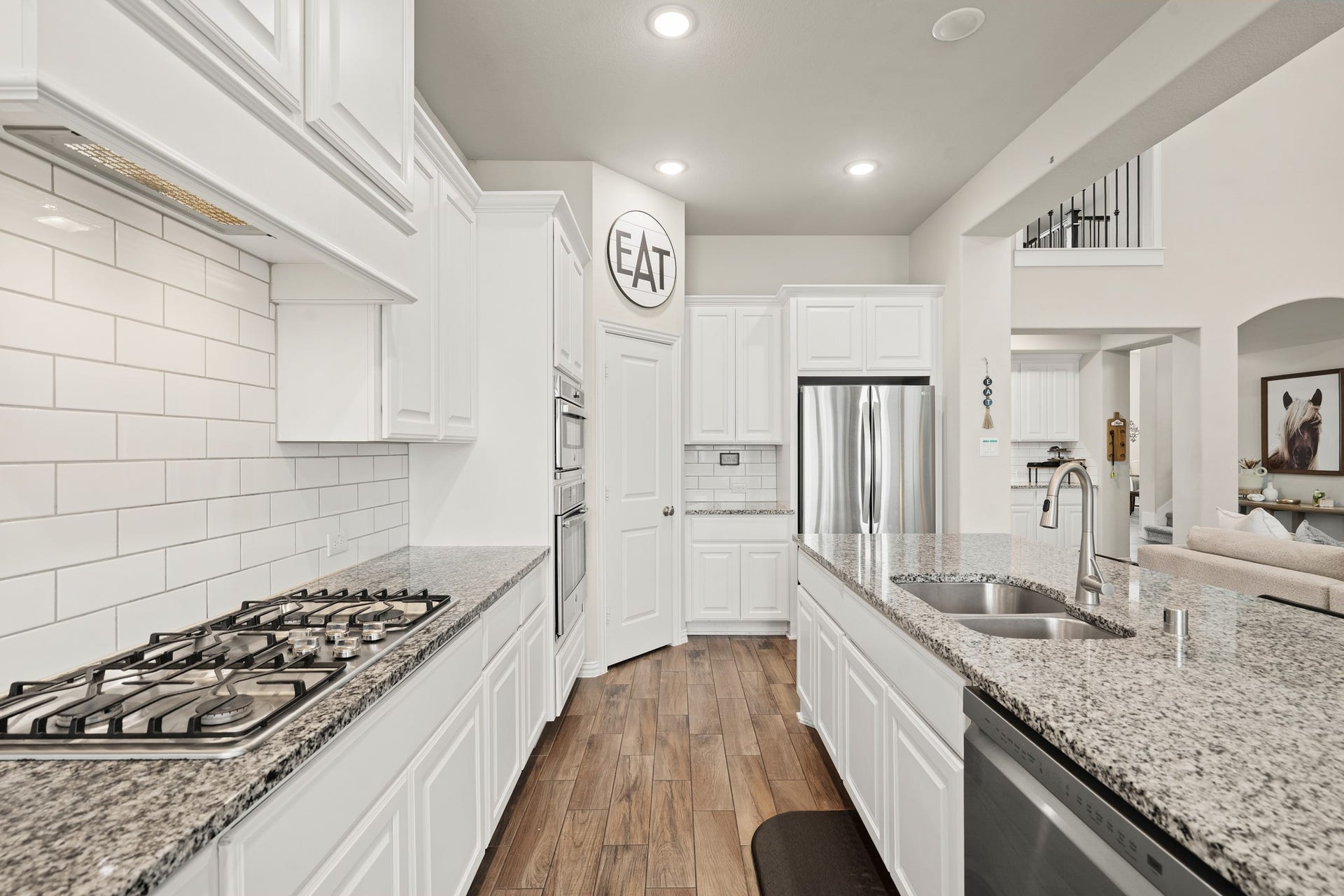 Alternative kitchen view showcasing the continuous flow of durable wood-look tile flooring, high-end stainless steel appliances, a gas cooktop, and a seamless connection to the main living spaces.
