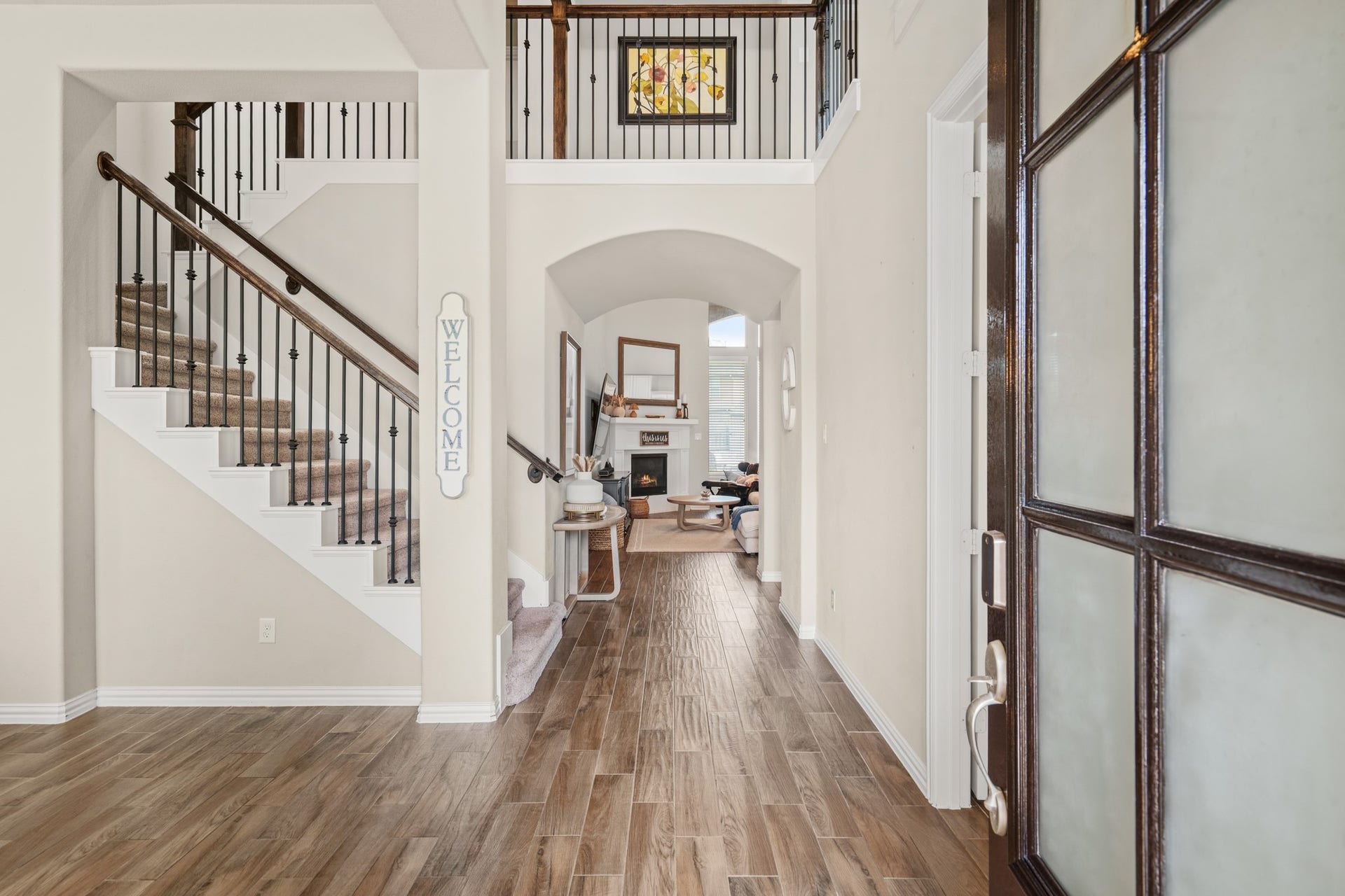 A grand grand entryway welcomes you with high-end wood-look tile flooring, an elegant iron-spindled staircase, and sweeping sightlines leading directly into the heart of the home.