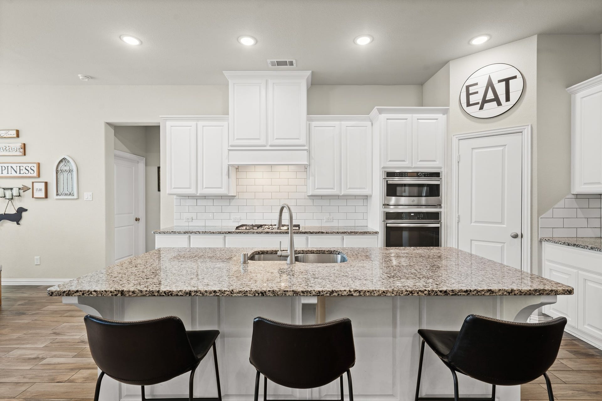 An entertainer's dream: The expansive gourmet island kitchen features a wide breakfast bar with modern seating, thick granite countertops, sleek white cabinetry, and a classic subway tile backsplash.