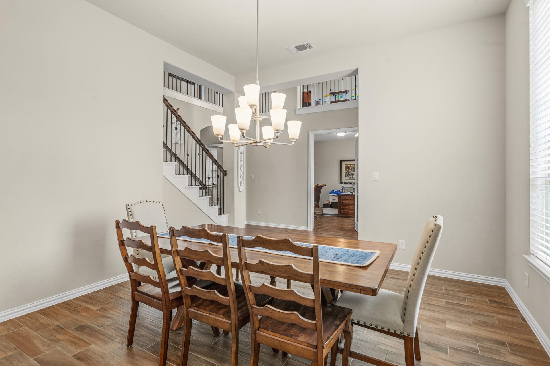 Designed with an open architectural flow, the elegant formal dining space offers beautiful sightlines straight to the upper-level wrought-iron balusters and the downstairs home office entry.