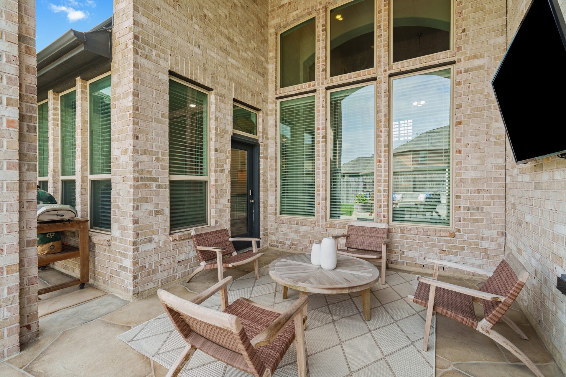 Framed by massive brick pillars and towering window walls, the soaring covered back patio provides a sheltered, high-ceiling outdoor living, complete with a TV & mount.