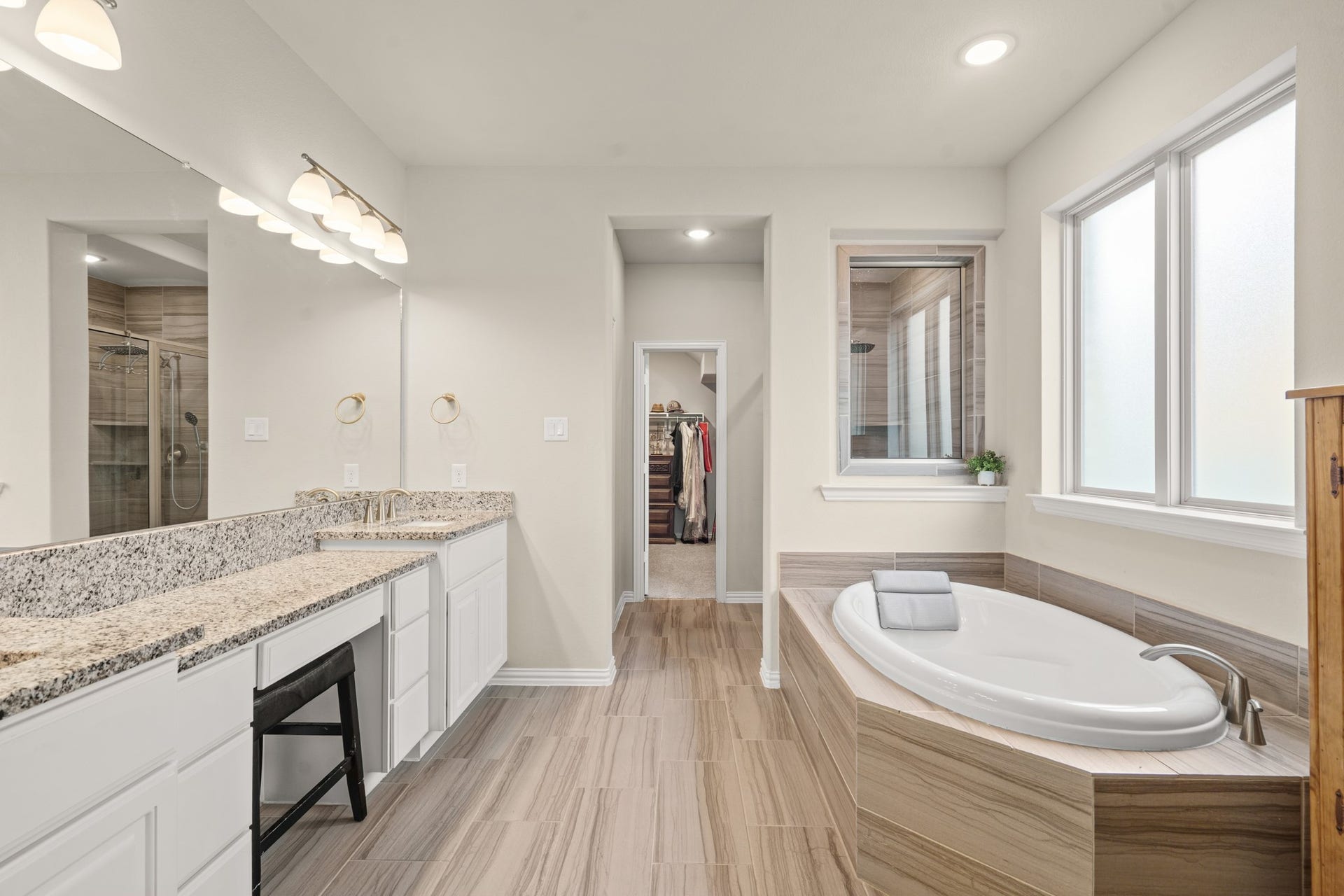 This wide view of the primary bath showcases its exceptional depth, revealing the entrance to the walk-in closet system and the glass entry to the separate shower.