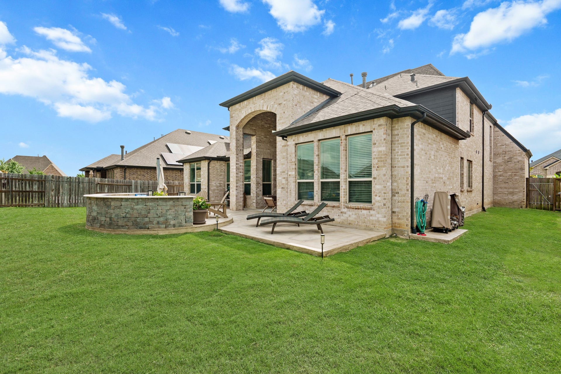 The expansive backyard oasis features a grand covered patio with soaring brick arches, and a sturdy custom stone firepit with seating area.