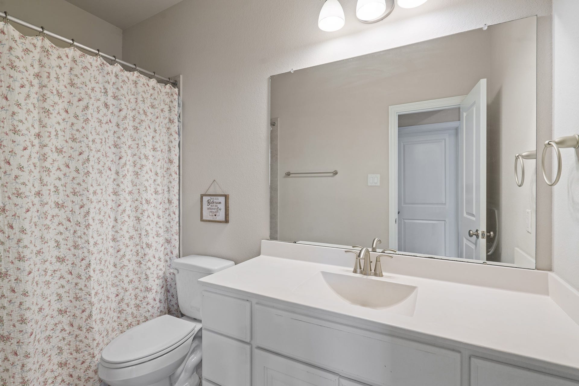 The downstairs secondary full bathroom features a bright, clean vanity space, a large matching mirror, and an adjoining shower and tub combination.