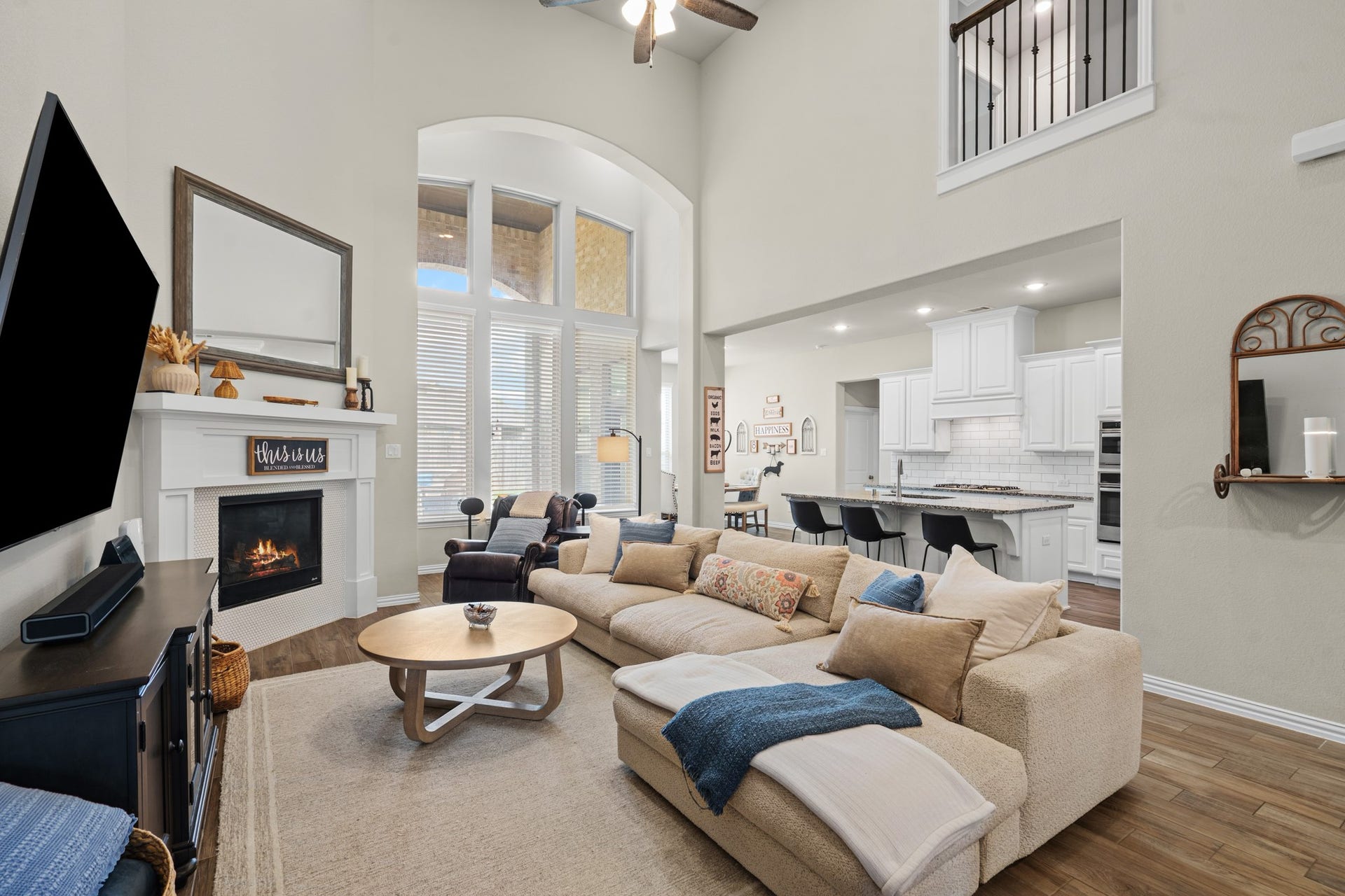 The spectacular, soaring two-story family room features a grand wall of arched windows, an elegant corner fireplace, and an expansive open-concept design.