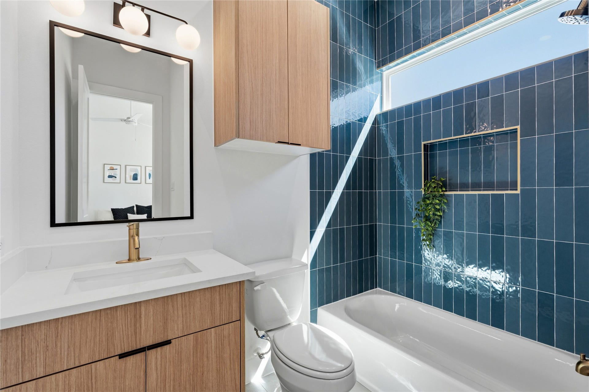 4610 Gunter Street, Houston, TX 77020 The architecture utilizes floor-to-ceiling blue vertical tiling in the tub-shower alcove to create a bold focal point. A light oak vanity and white stone countertop are accented by brushed gold hardware and modern globe lighting.