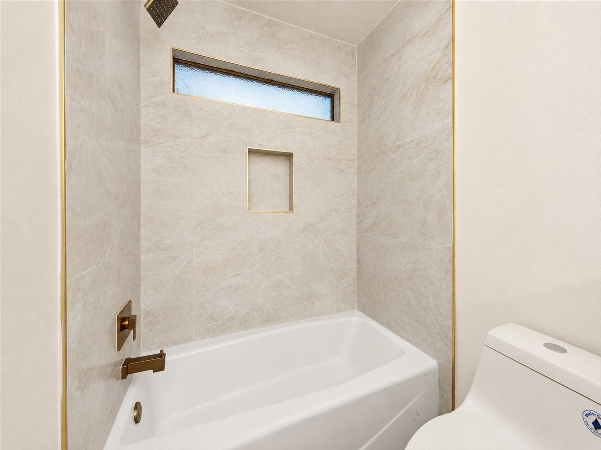 Renovated tub and shower combination features floor-to-ceiling tile, modern fixtures, a rainfall showerhead and built-in niche, creating a fresh, polished space designed for comfortable everyday routines.