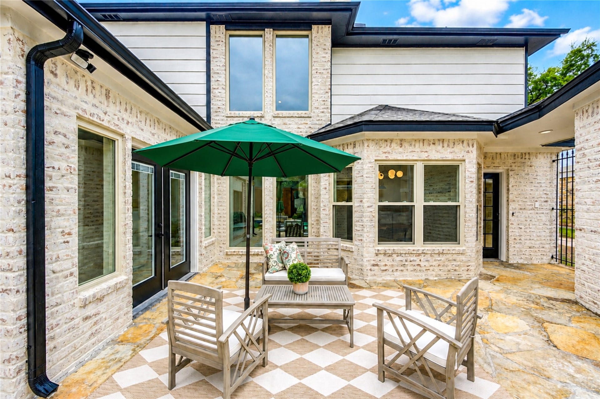 Another view of the private courtyard highlights the homes inviting indoor-outdoor connection, with French doors and expansive windows opening the living spaces to the patio. Surrounded by distinctive German schmear brick, its a charming setting for morning coffee, alfresco meals, evening cocktails or relaxed conversation with friends.