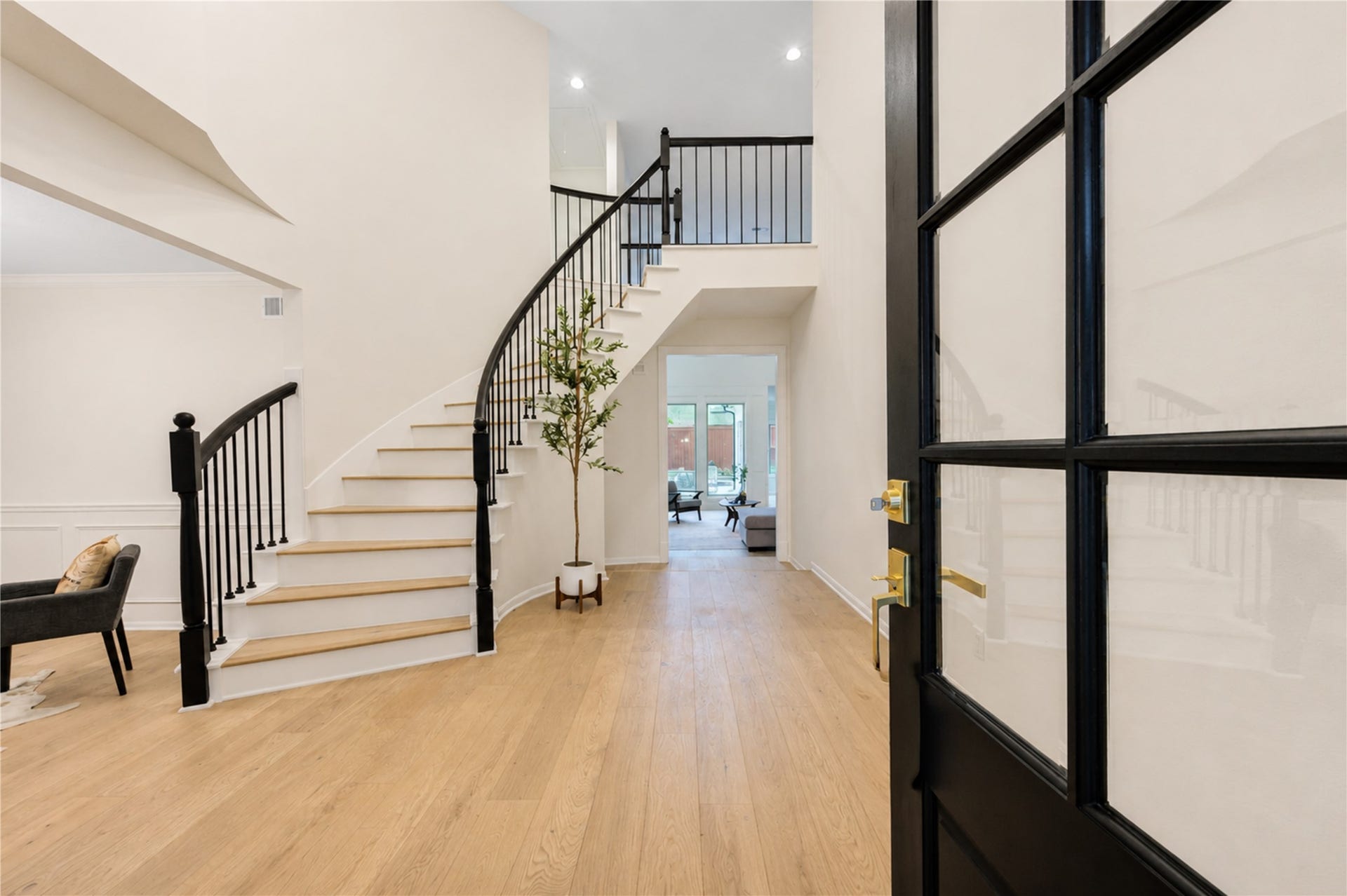 Stylish entry hall featuring warm French Oak floors, a dramatic staircase and modern black-framed glass doors, creating a polished first impression and seamless flow into the home.