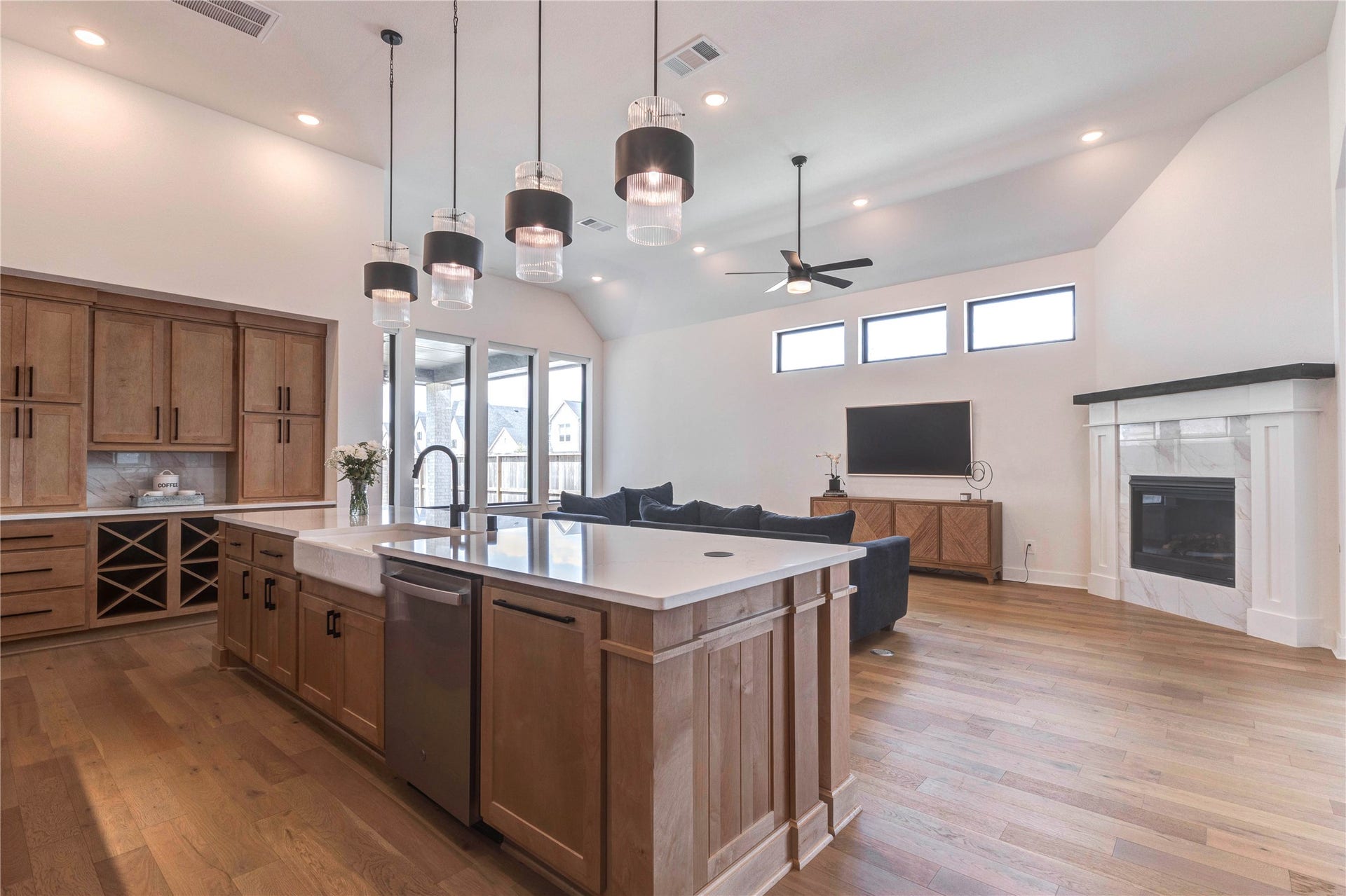 4510 Windmill Landing Lane, Fulshear, TX 77441 This modern living space features an open floor plan with a spacious kitchen island, elegant pendant lighting, and a cozy living area with a fireplace. Large windows provide natural light, enhancing the airy feel.
