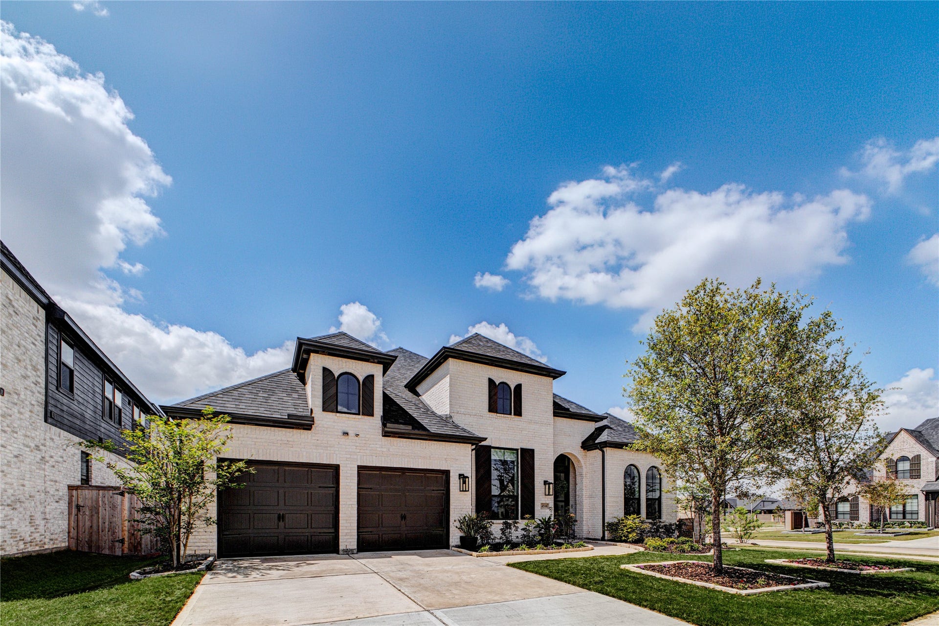 4510 Windmill Landing Lane, Fulshear, TX 77441 Modern 1 story brick home with a three-car garage, arched windows, and a well-maintained front yard featuring a tree. The house is in a corner lot.