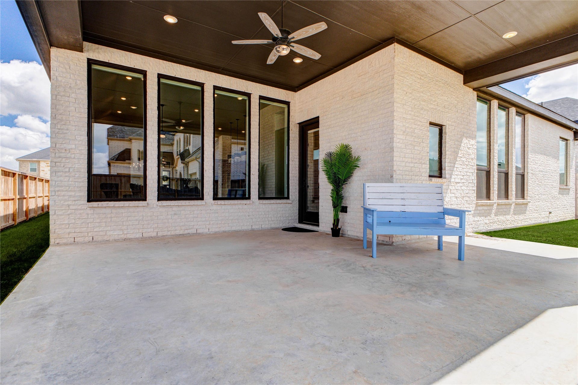 4510 Windmill Landing Lane, Fulshear, TX 77441 Spacious covered patio with a ceiling fan, perfect for outdoor relaxation. It features large windows that provide ample natural light, a light brick exterior, and a neatly maintained lawn, creating an inviting outdoor living space.