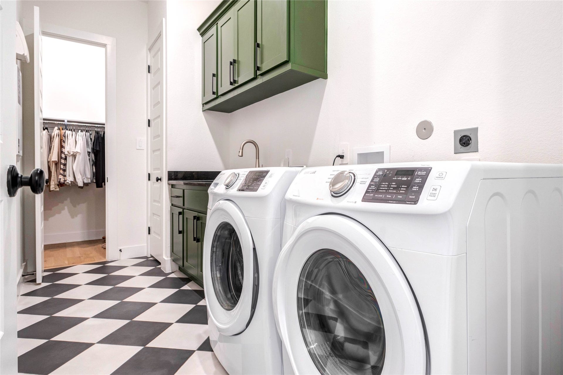 4510 Windmill Landing Lane, Fulshear, TX 77441 This laundry room features stylish green cabinetry, a sleek black countertop, and modern appliances. The space is well-lit and has a checkered floor, offering a functional and attractive area for laundry tasks. Including a sink