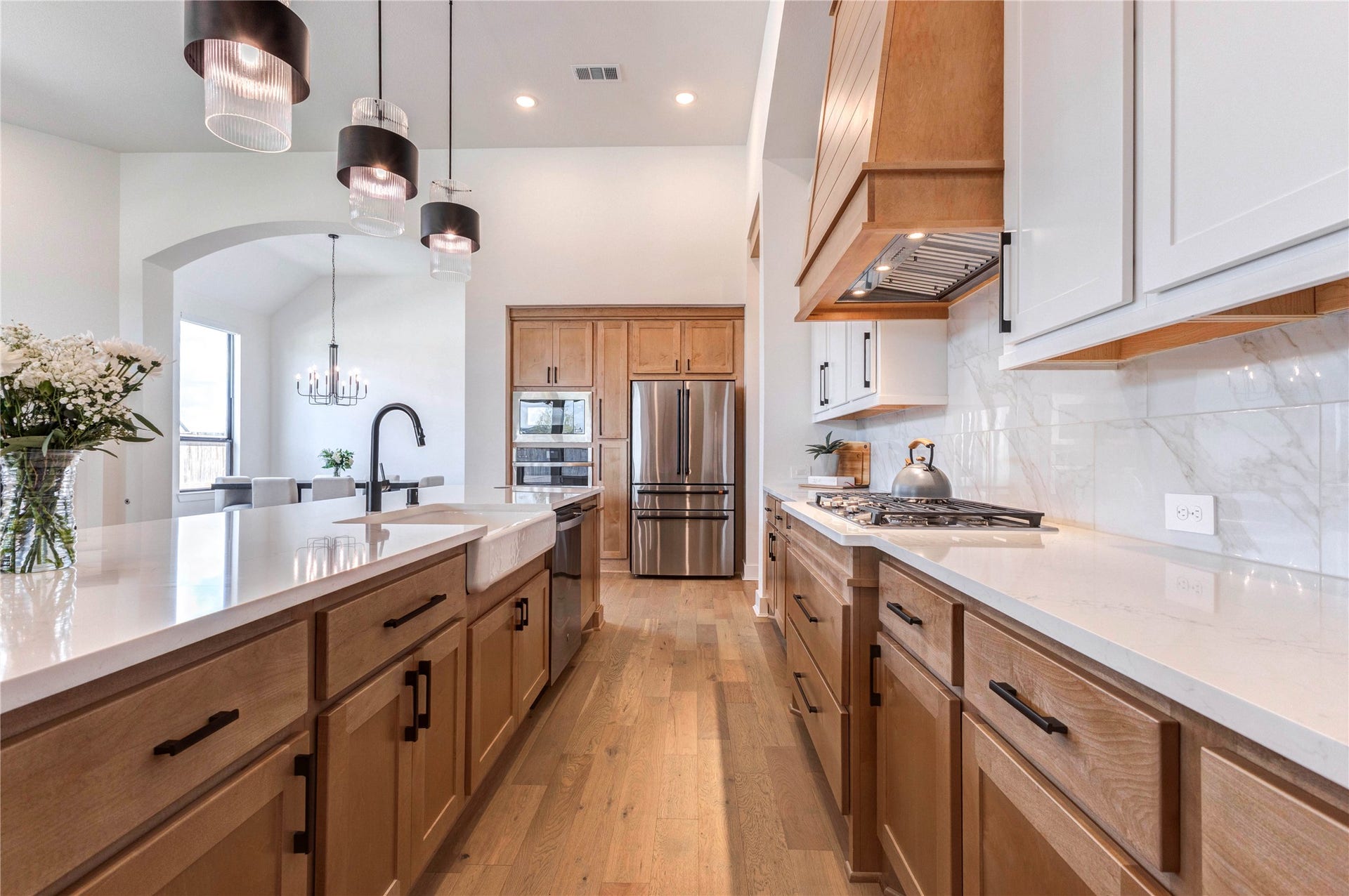 4510 Windmill Landing Lane, Fulshear, TX 77441 Spacious kitchen with a large island, elegant pendant lighting, and a mix of wood and white cabinetry. It features stainless steel appliances, a stylish range hood, and a bright, airy feel with plenty of natural light.