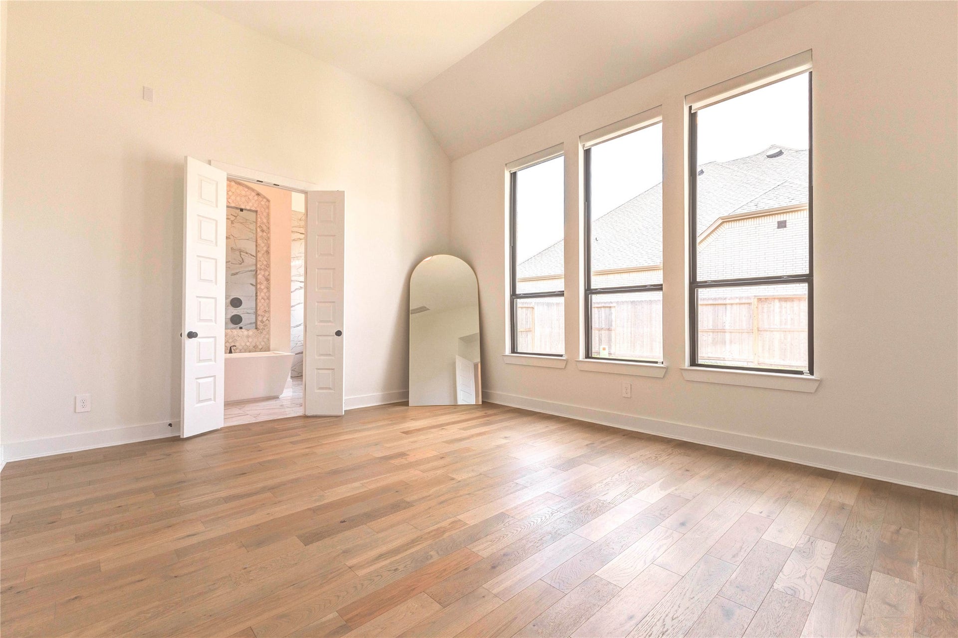 4510 Windmill Landing Lane, Fulshear, TX 77441 This spacious, bright room features large windows, hardwood floors, and a vaulted ceiling. It connects to a bathroom with double doors, adding convenience and elegance.