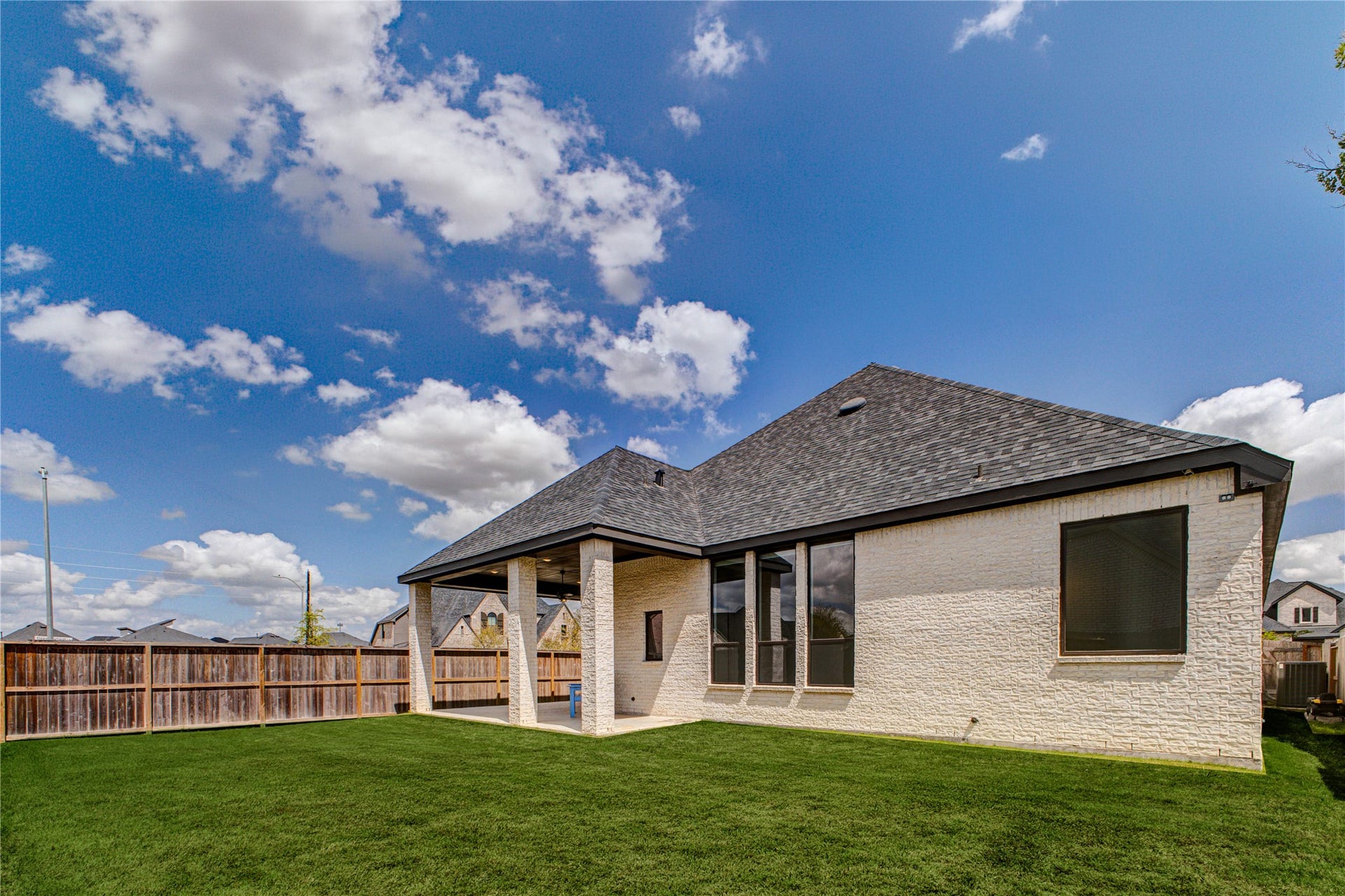 4510 Windmill Landing Lane, Fulshear, TX 77441 Modern, single-story home with a neatly maintained lawn, a covered patio, and a fenced backyard. The exterior features light brickwork and large windows, offering a spacious and inviting outdoor space under a clear blue sky.