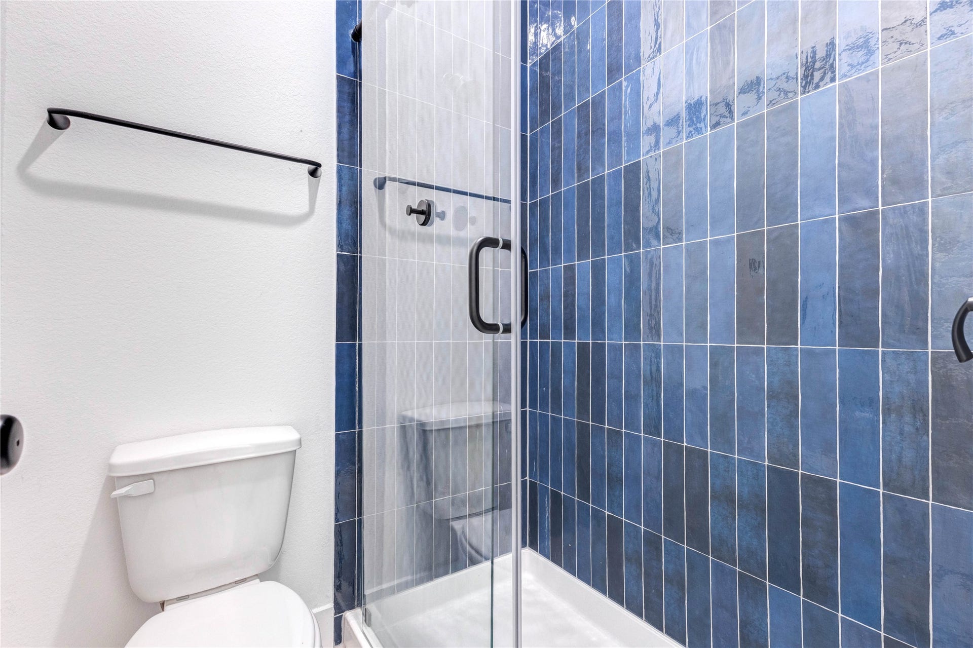 4510 Windmill Landing Lane, Fulshear, TX 77441 This bathroom features a sleek, modern design with a double vanity in deep blue tile, black fixtures, and a large mirror. The space is bright with white walls and wood flooring, offering a clean, stylish look.