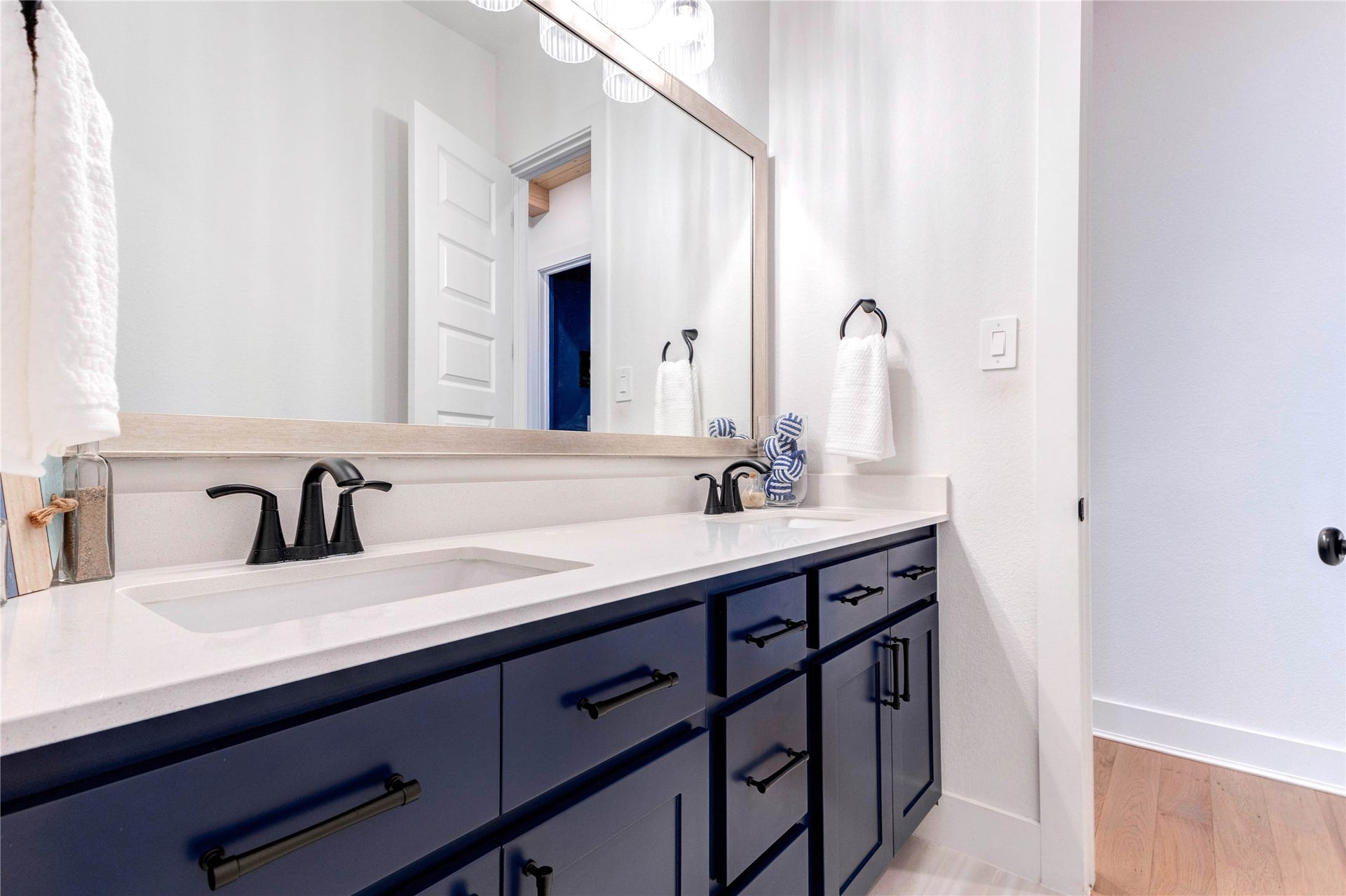 4510 Windmill Landing Lane, Fulshear, TX 77441 This modern bathroom features a double sink with sleek black fixtures, navy blue cabinetry, and a large mirror. It includes a separate toilet area and a shower with dark blue tiles, offering a clean and stylish look.