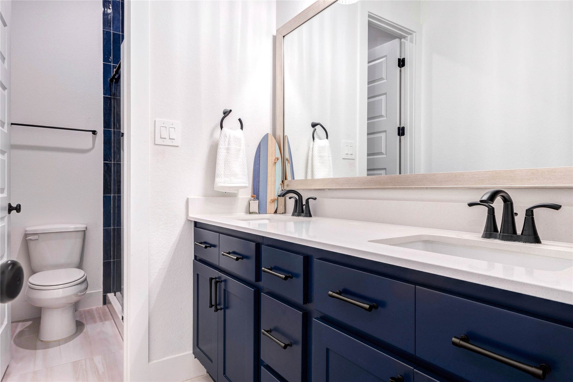 4510 Windmill Landing Lane, Fulshear, TX 77441 This modern bathroom features a double sink with sleek black fixtures, navy blue cabinetry, and a large mirror. It includes a separate toilet area and a shower with dark blue tiles, offering a clean and stylish look.