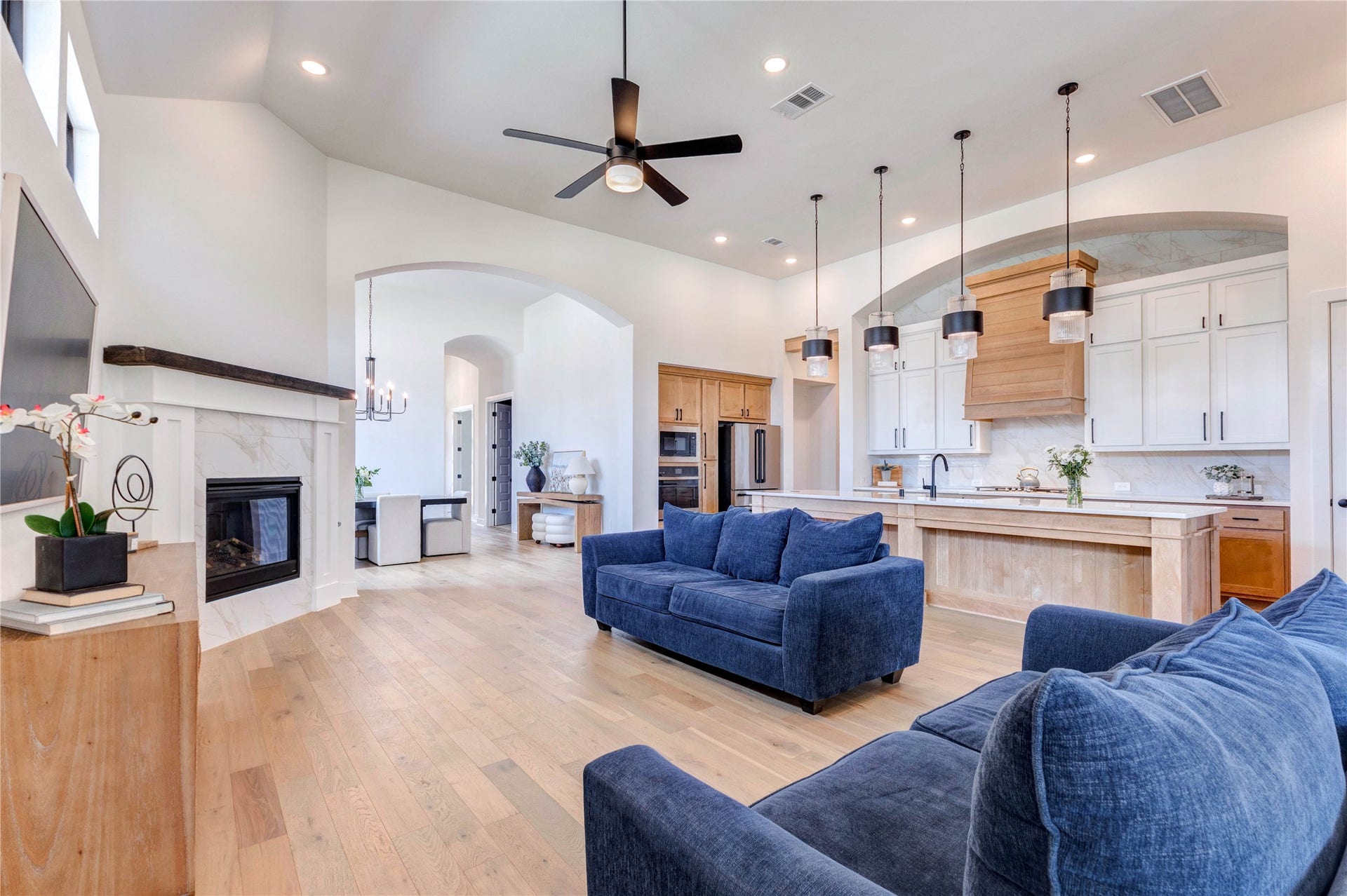4510 Windmill Landing Lane, Fulshear, TX 77441 This spacious living area features an open floor plan with high ceilings, modern lighting, and large windows that allow natural light to flood in. It includes a cozy fireplace, stylish wood flooring, and a sleek kitchen with stainless steel appliances and a large island. The room is elegantly furnished with comfortable seating and tasteful decor.