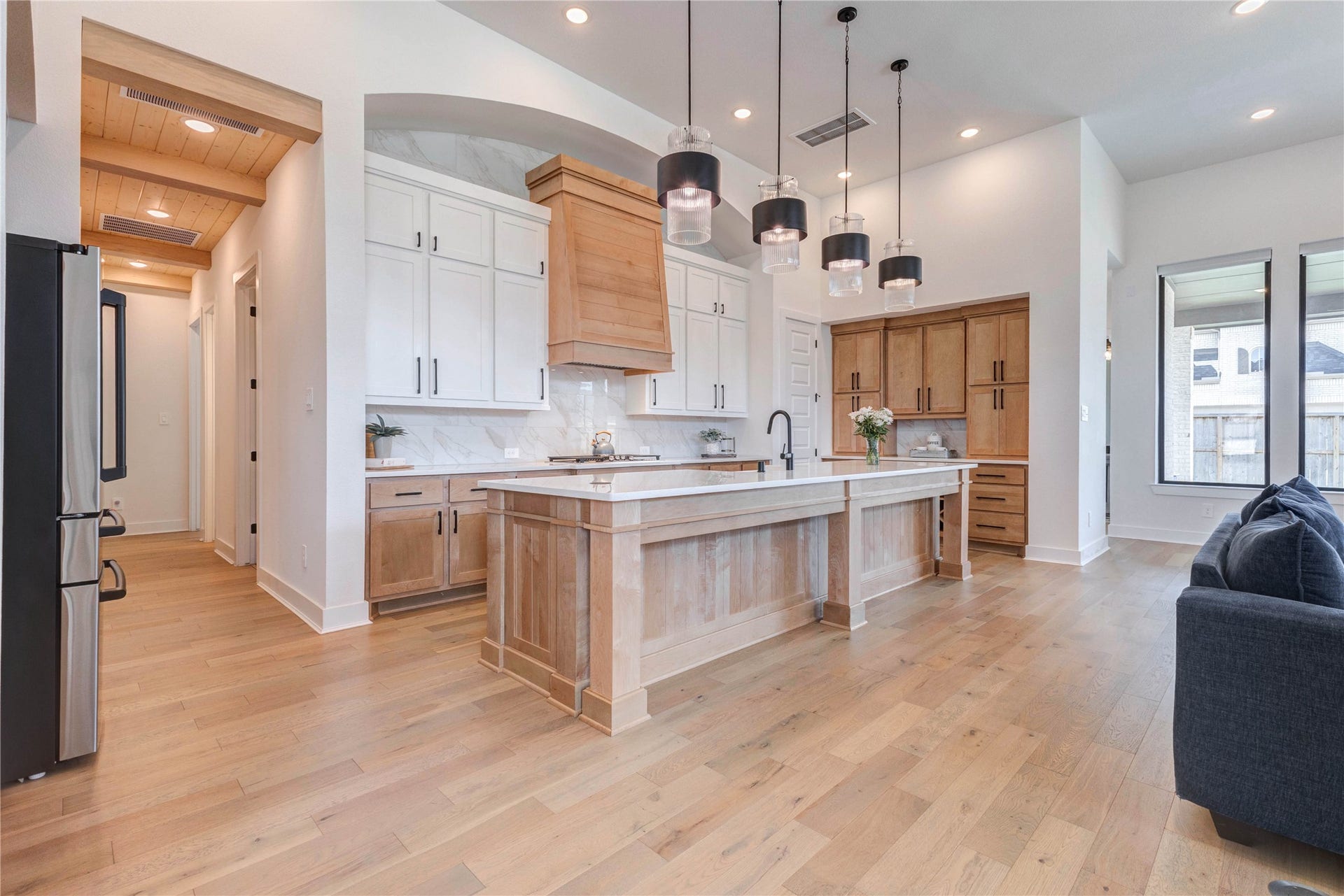 4510 Windmill Landing Lane, Fulshear, TX 77441 Modern kitchen features a spacious, open layout with light wood flooring, a large central island, and sleek cabinetry. Pendant lights add elegance, while stainless steel appliances and ample natural light enhance functionality and ambiance.