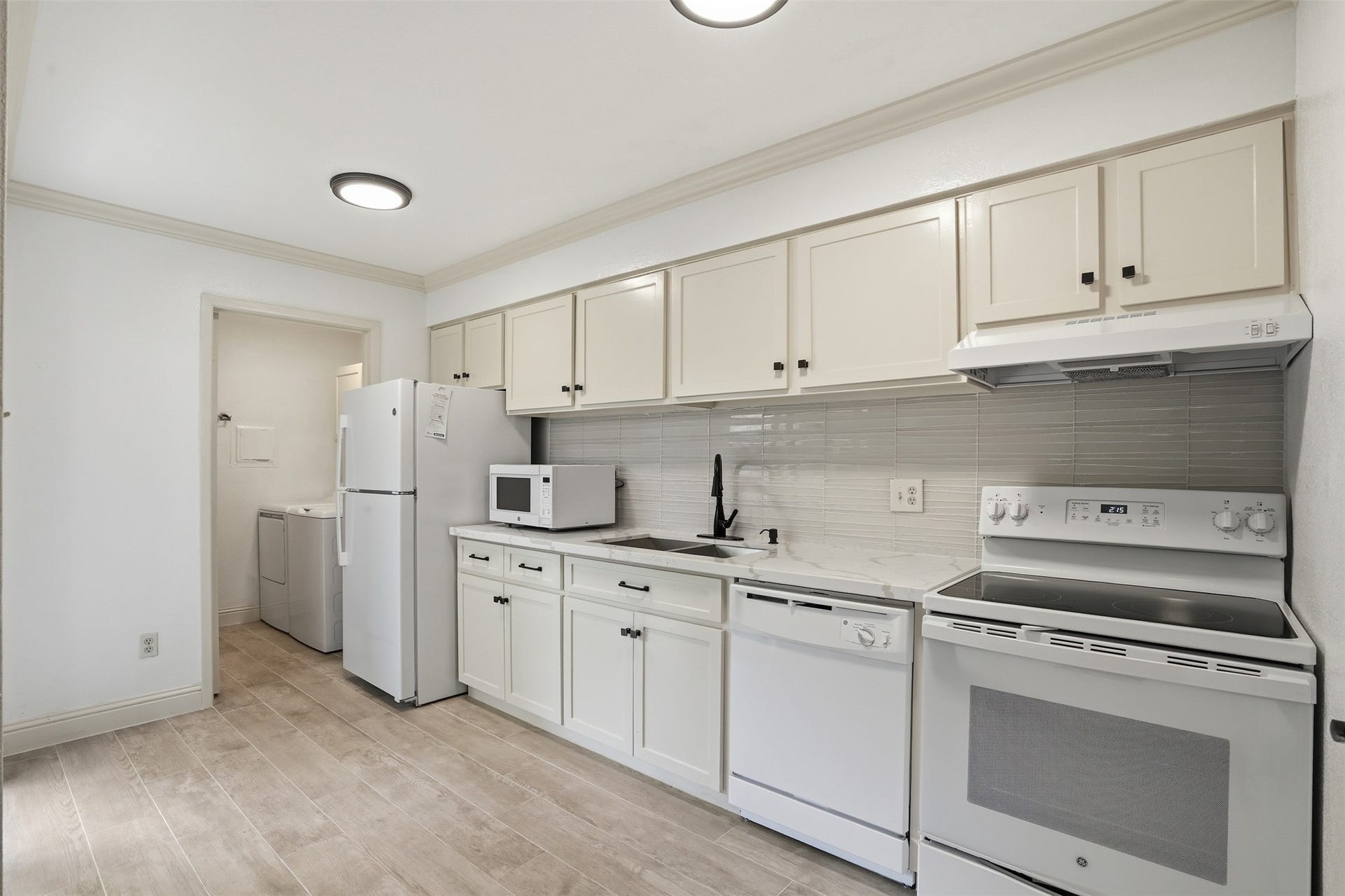 Kitchen featuring a bit off white cabinetry, beautiful quartz counter space, new wlwgnt tile backsplash and an adjacent utility room.