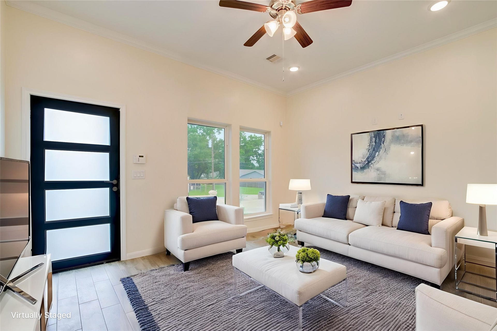 This modern living room features a sleek design with neutral walls and tile flooring, a ceiling fan, and ample natural light through large windows.