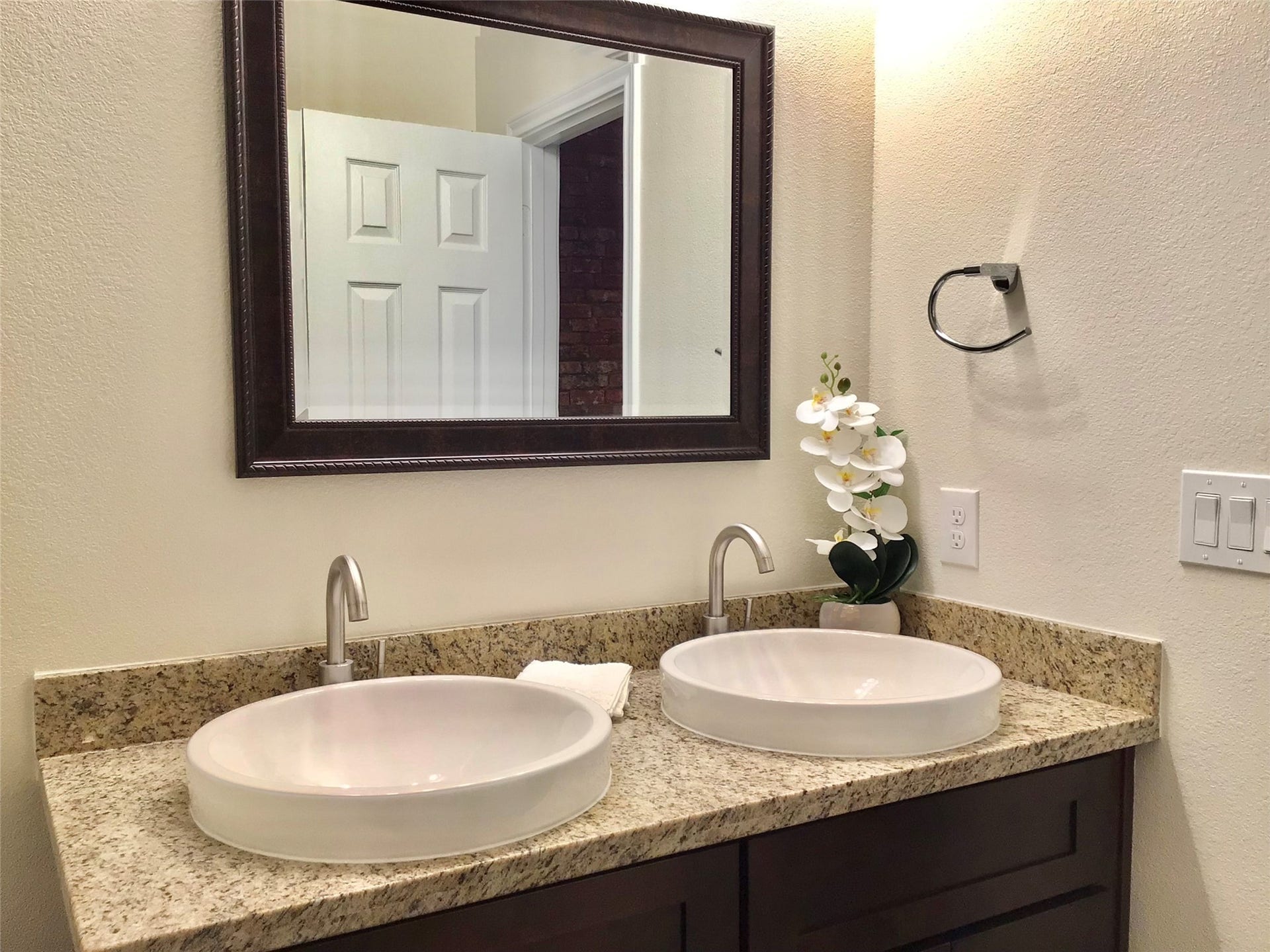 Primary bathroom features a dual sink vanity with elegant vessel sinks and sleek faucets. The granite countertop adds a touch of luxury, complemented by a large framed mirror.