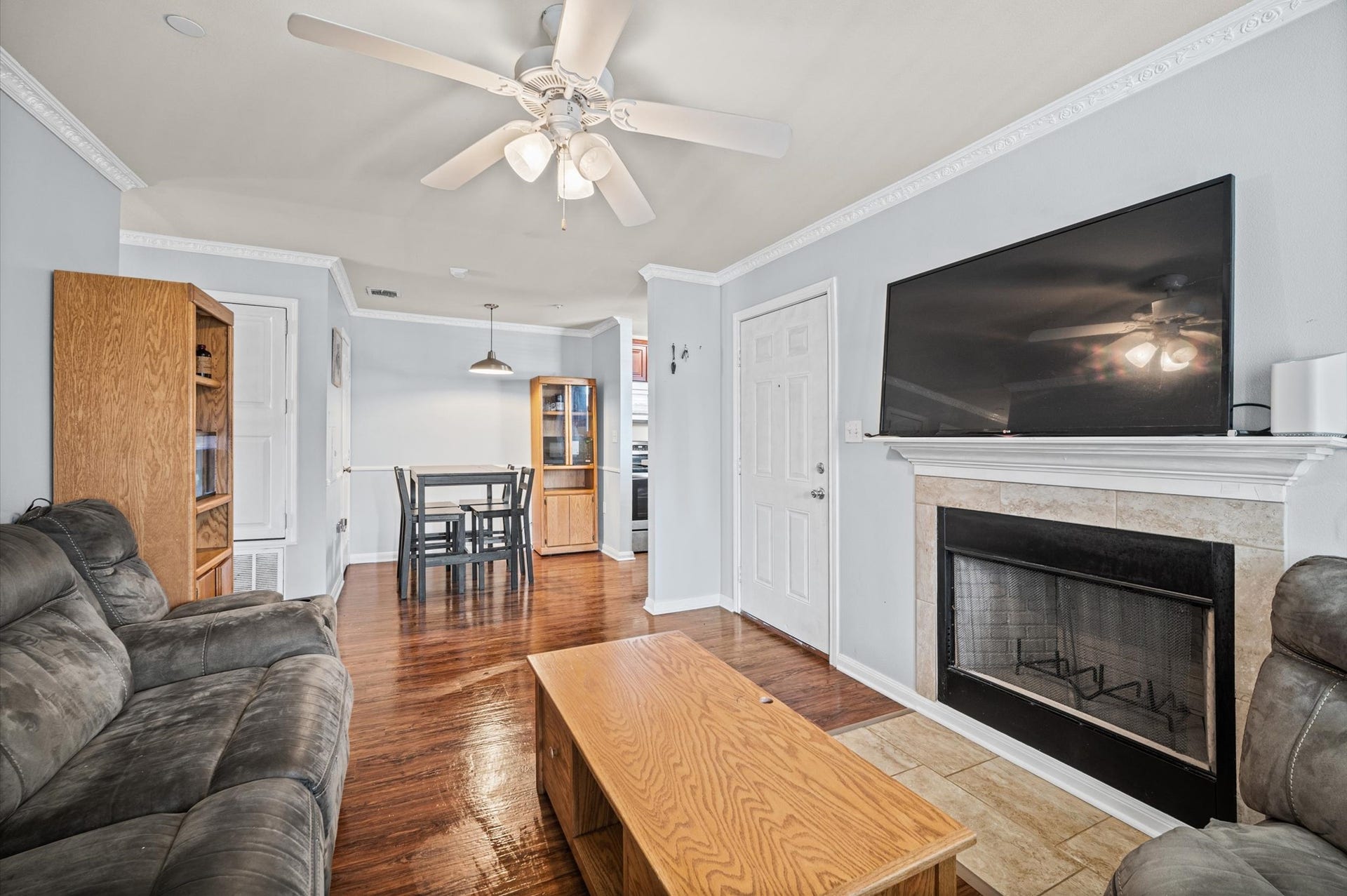 7600 Emmett F Lowry Expressway, #416, Texas City, TX 77591 Cozy living space with a ceiling fan, featuring a fireplace. The open layout flows into a dining area and kitchen, accented by wood flooring and built-in shelving.