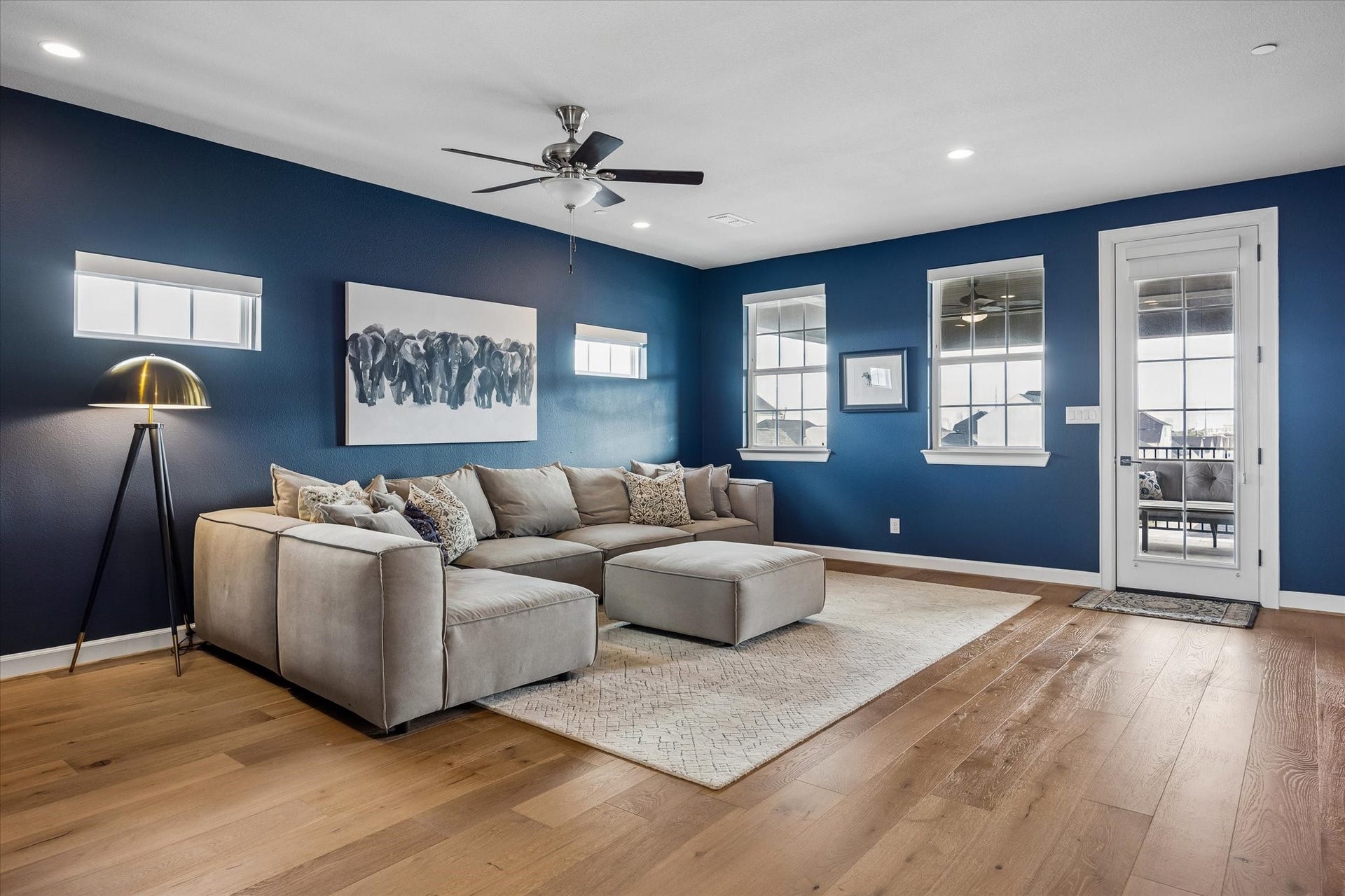 Sophisticated navy walls and warm wood floors define the versatile game room. Featuring recessed lighting and custom Hunter Douglas shades, the space offers a seamless transition to the covered deck.