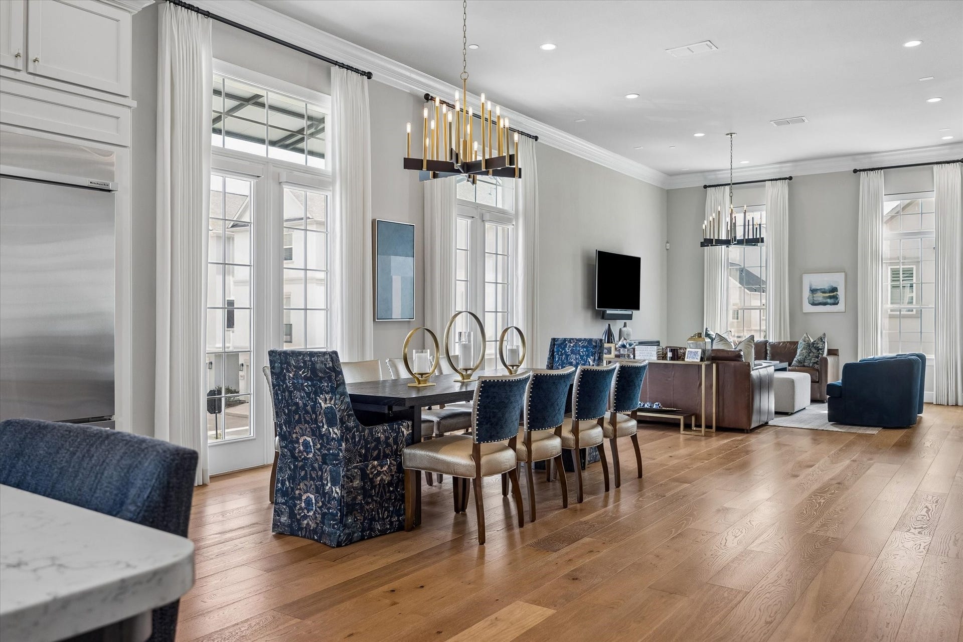 The heart of the home presents a seamless, open-concept space. Filled with natural light, the rooms feature many windows with elegant transoms and electric Hunter Douglas shades. Custom chandeliers add a touch of timeless sophistication to the airy atmosphere. Note the rich wood floors that continue throughout much of the home.