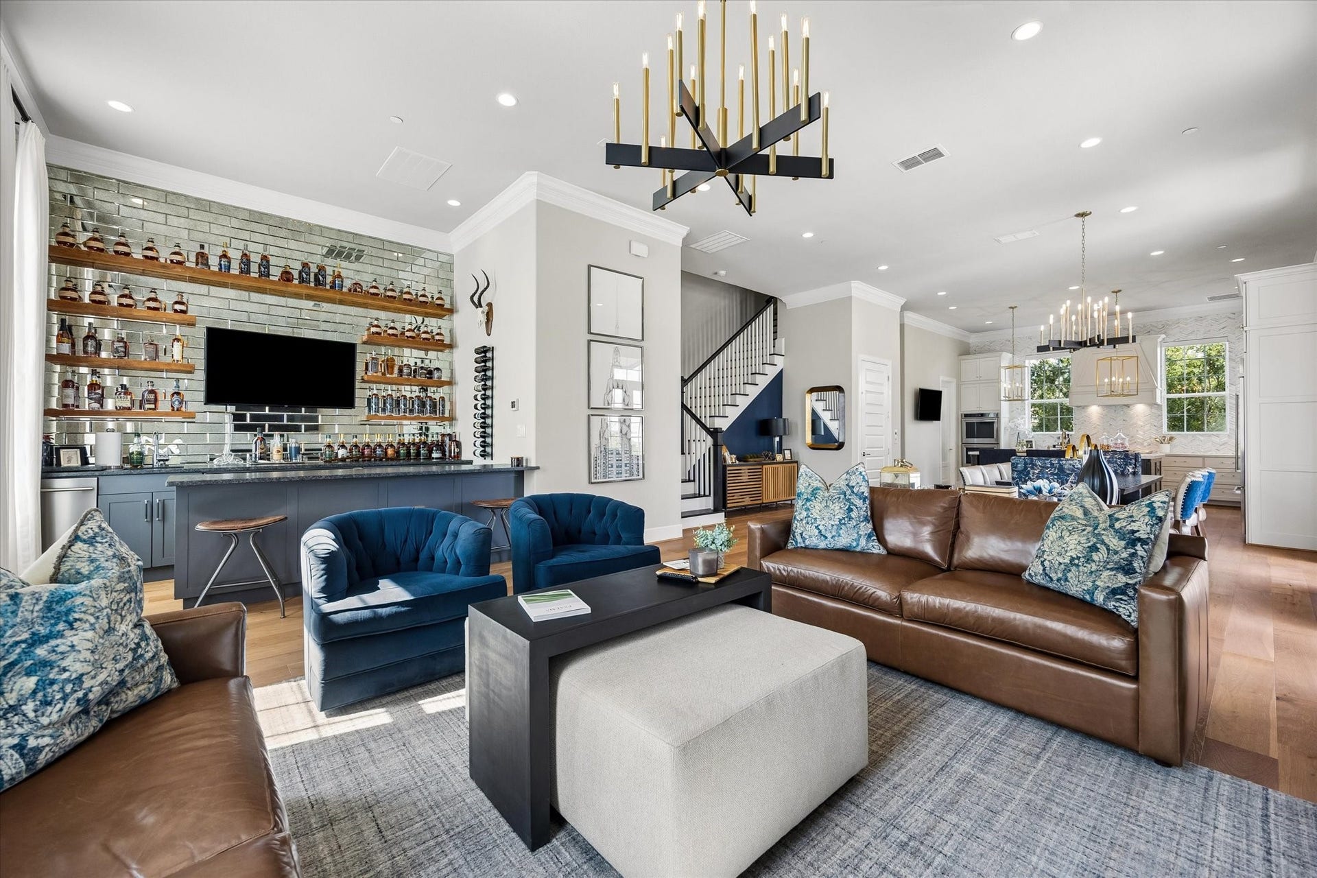 The living room flows effortlessly into a sophisticated wet bar designed for the ultimate host. The space stands out with mirrored subway tile backsplash, granite countertops, floating wood shelves, a dedicated ice maker, and dual wine and beverage fridges.