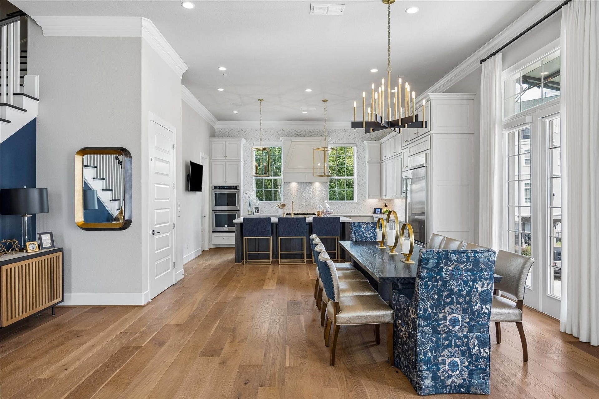 Sunlight pours through double-stacked windows with transom accents, framing an elegant dining space anchored by a custom chandelier. With its seamless flow into the kitchen and living areas, this room is perfectly designed for hosting and effortless entertaining.