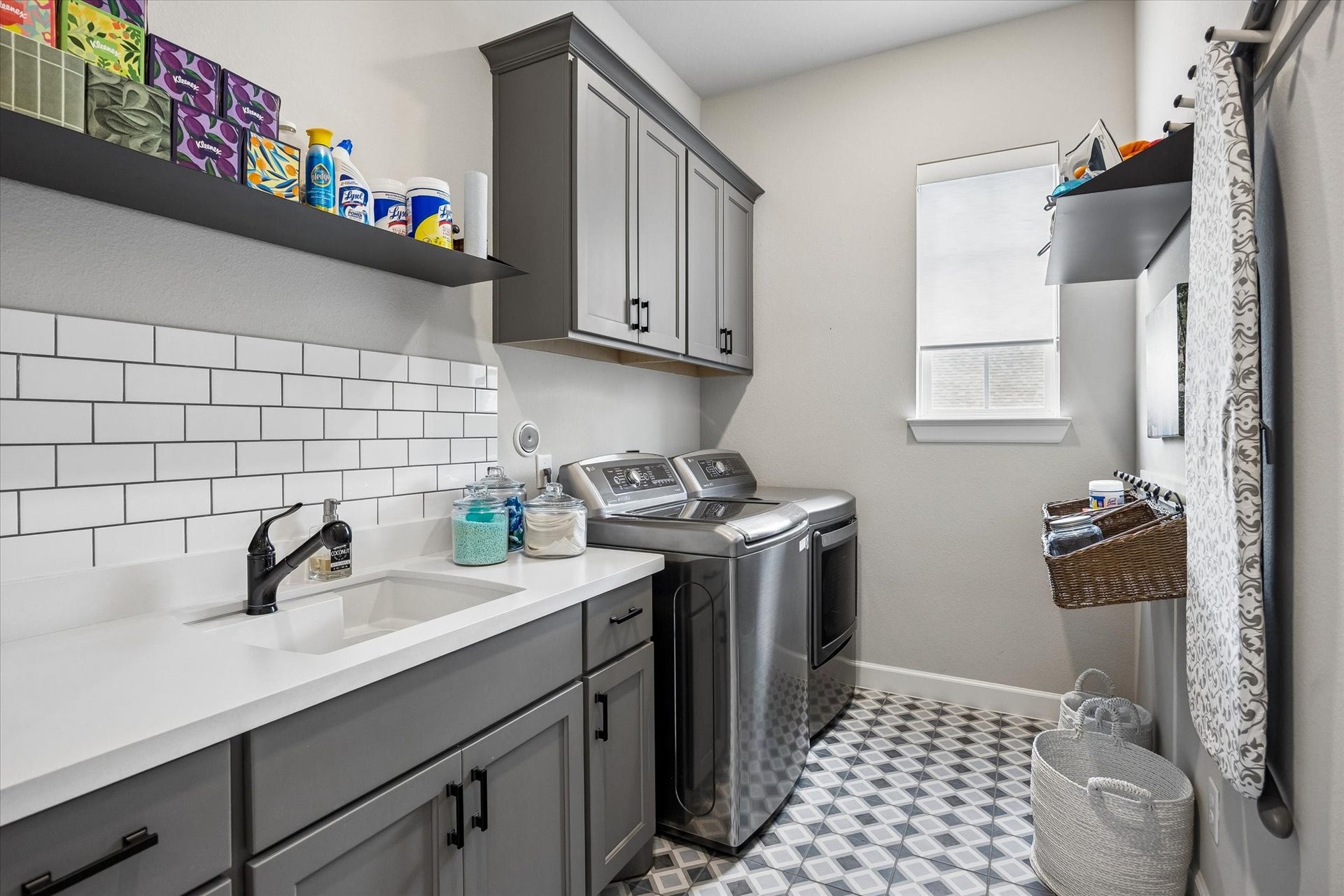 The laundry room, conveniently situated on the same level as the primary suite, features sink with classic subway tile backsplash, and plenty of storage within the upper and lower cabinets. The charming patterned floor tile adds a pop of personality to this functional and beautifully designed room.