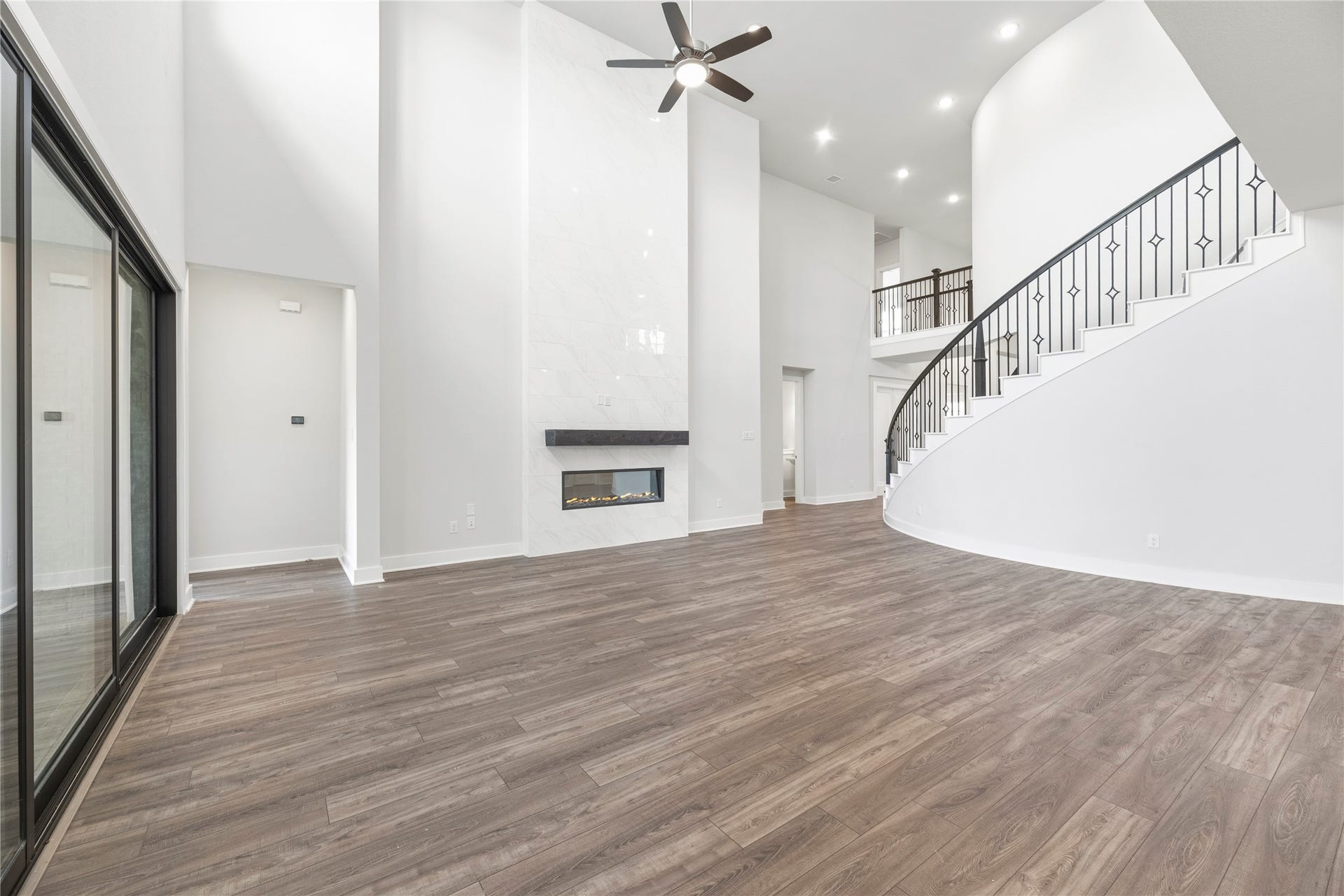 10314 Forest Lake Drive, Missouri City, TX 77459 Angle showcasing the sleek linear fireplace, wood-look plank flooring, grand curved staircase with wrought-iron railing, and large sliding glass patio doors.